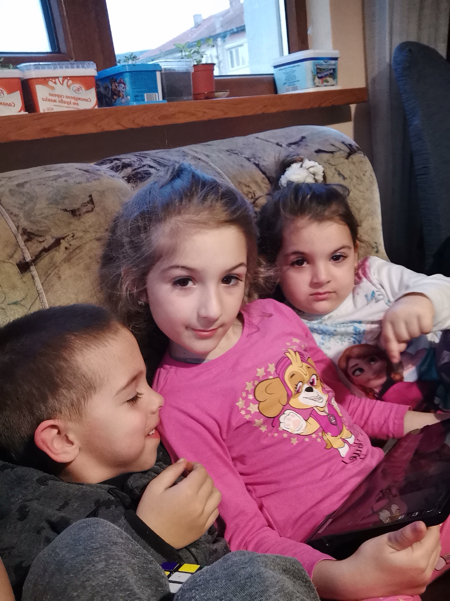 Three children sit together on sofa in Bulgarian home