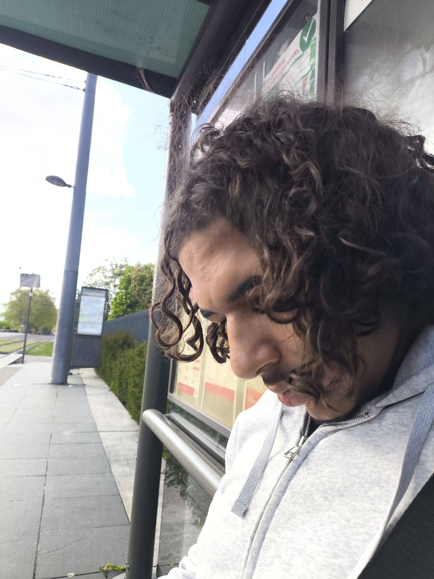Person in grey hoodie waits at urban bus stop