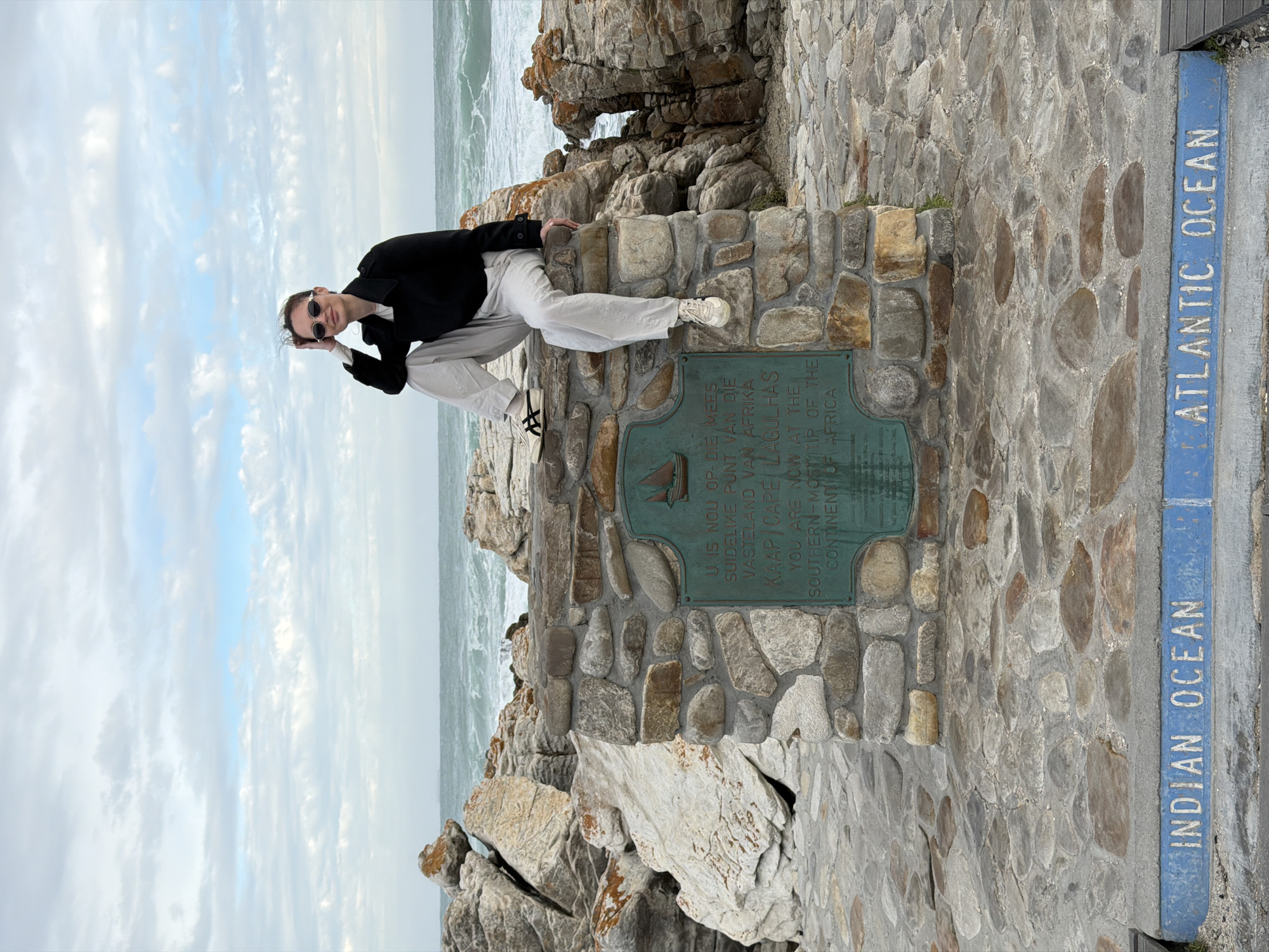 Tourist poses at stone monument in Cape Agulhas