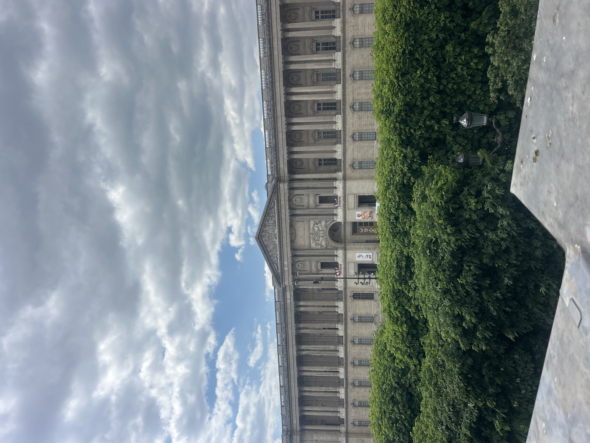 Classical building photographed amid green trees under cloudy sky
