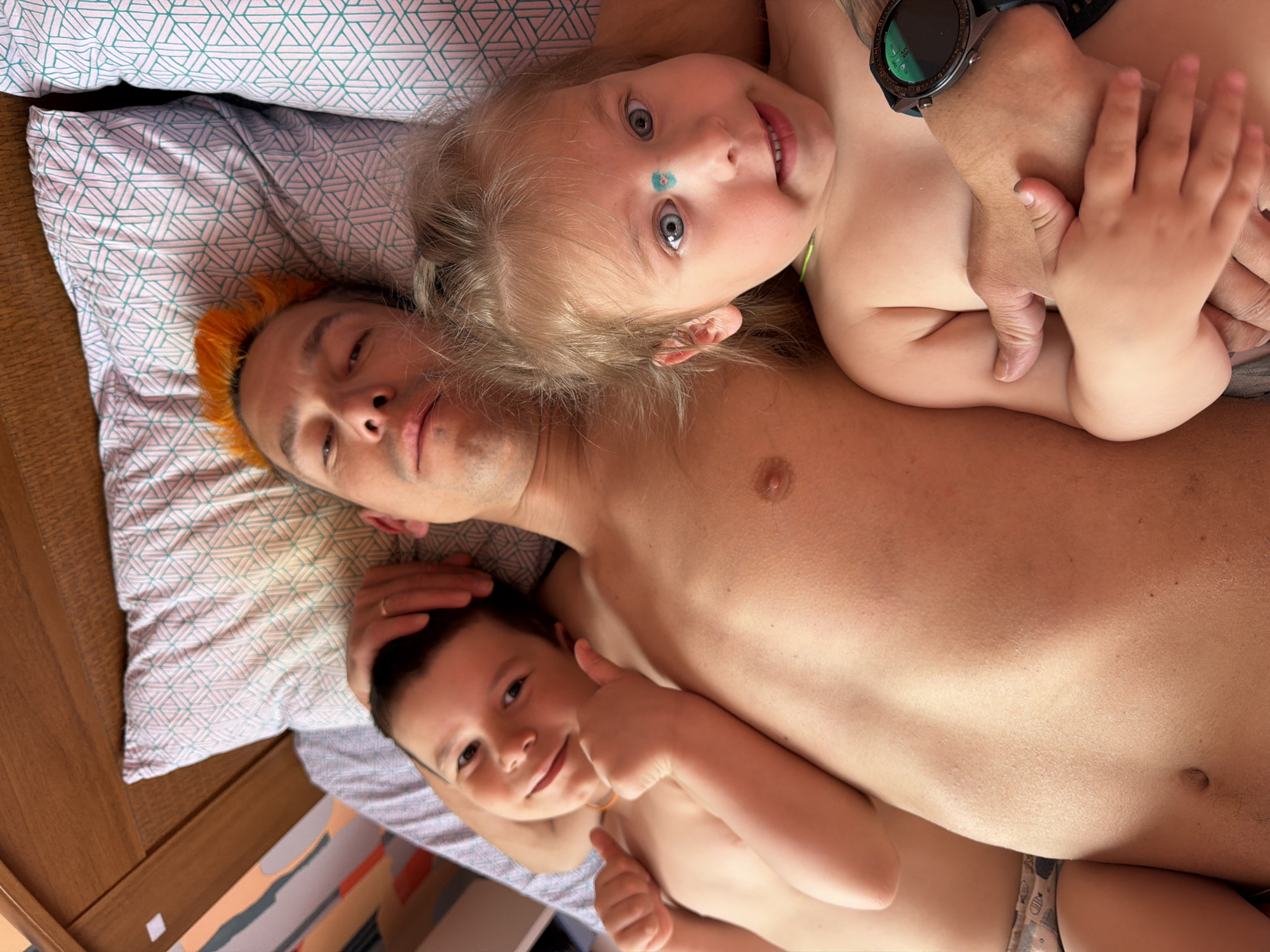 Three people rest together on geometric-patterned bed
