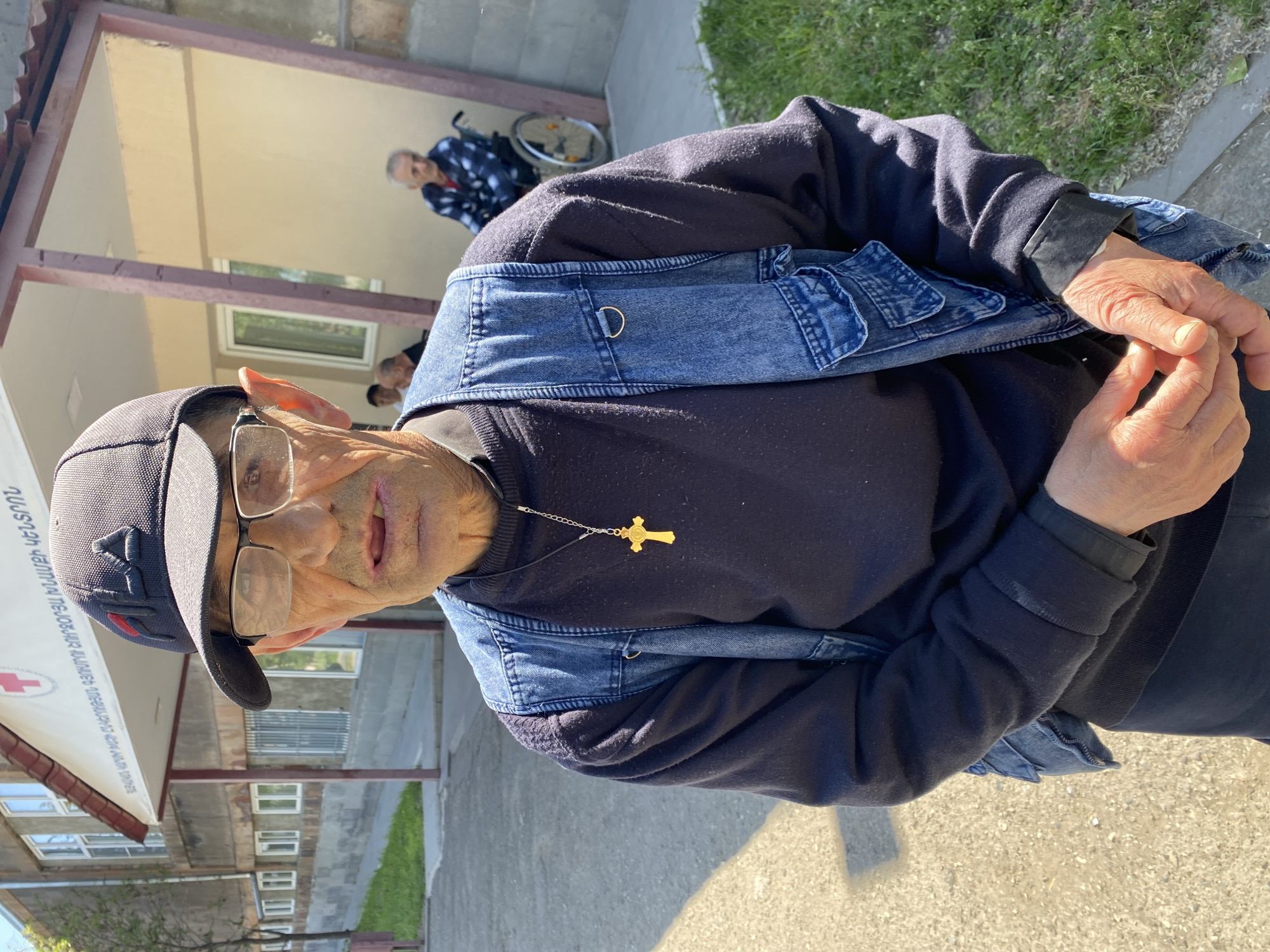 Denim vest and gold cross outside a Gyumri building
