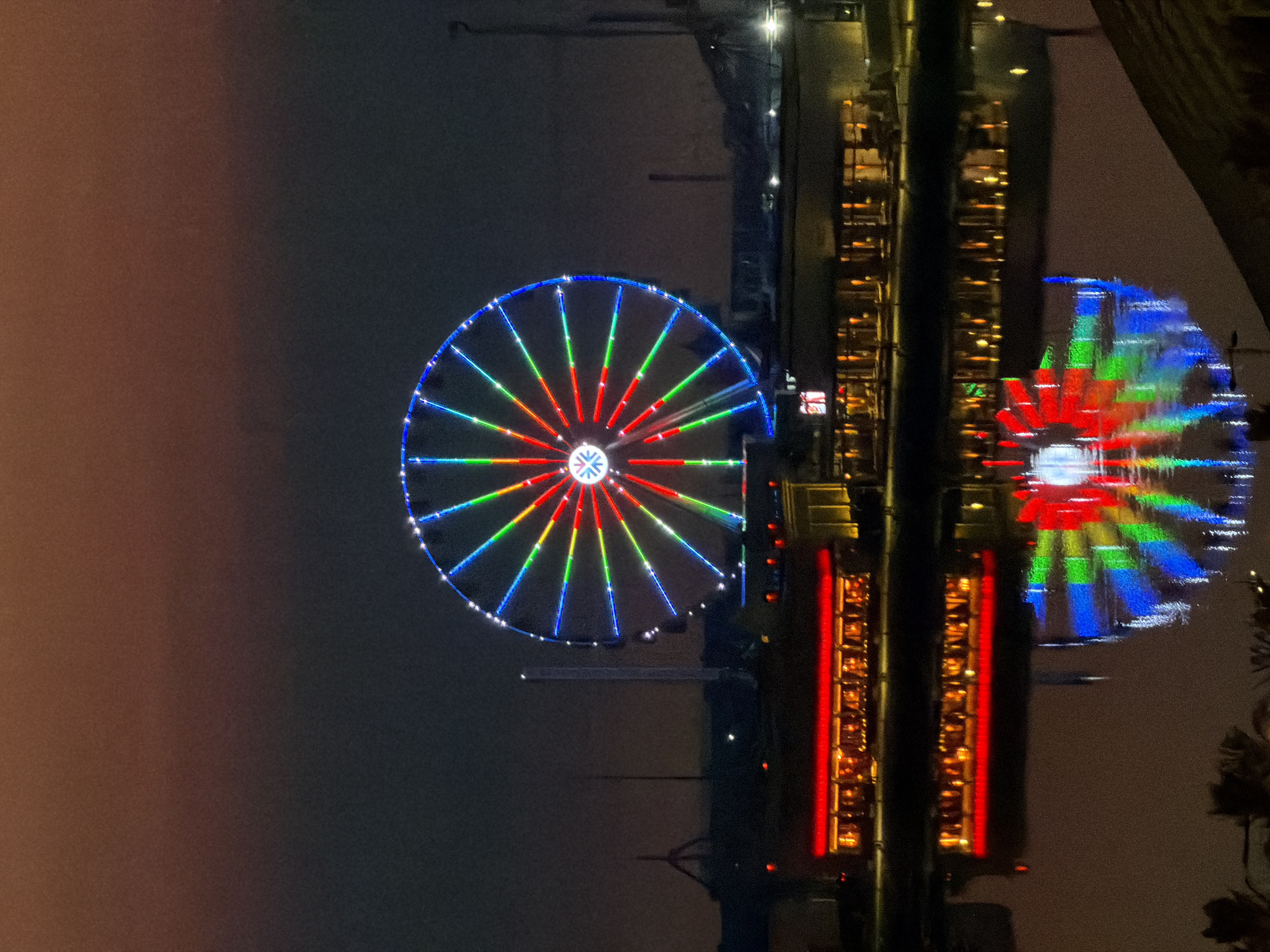 Lit Ferris wheel anchors a waterfront city at dusk