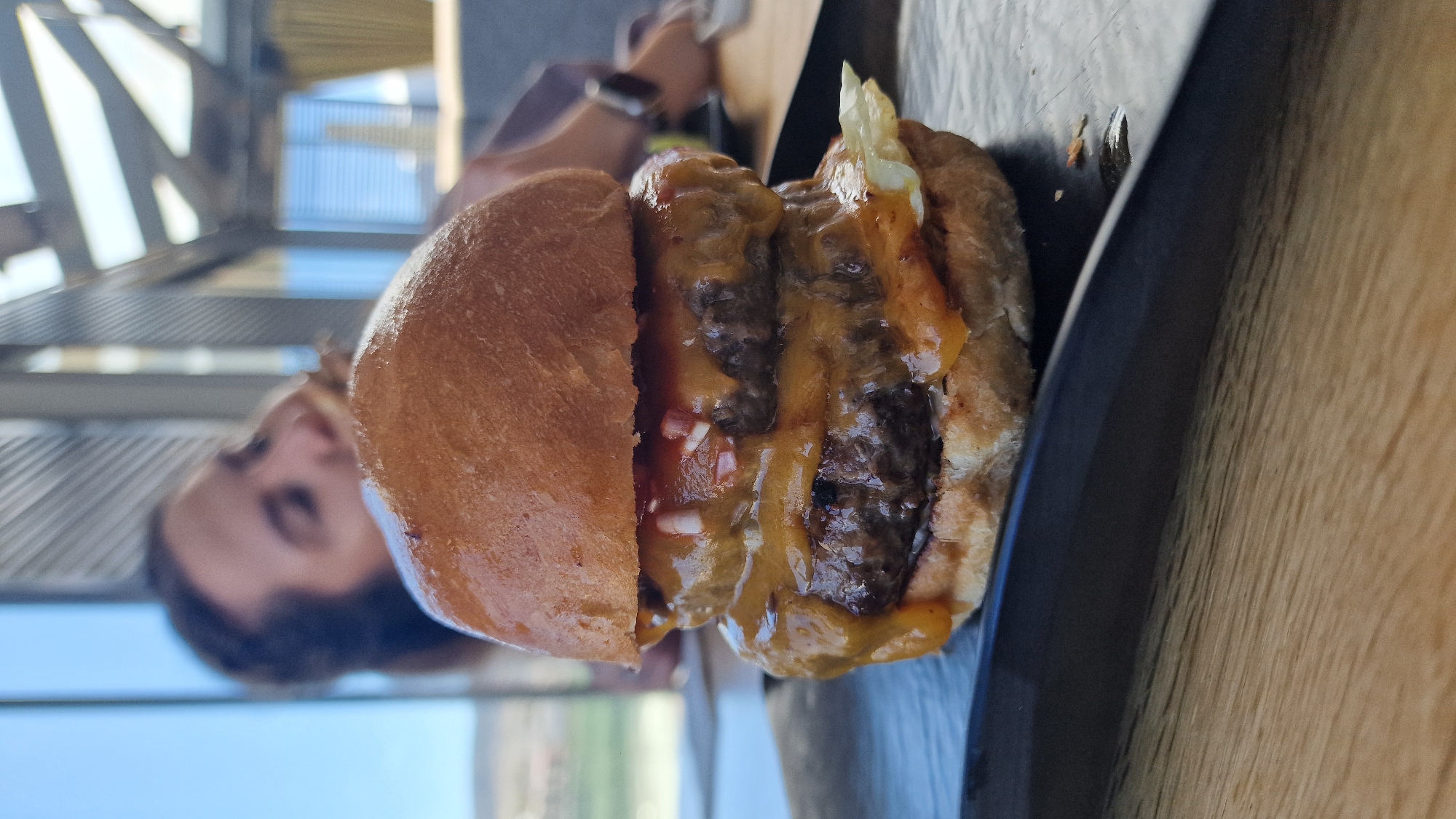Half-finished double cheeseburger observed on wooden table surface