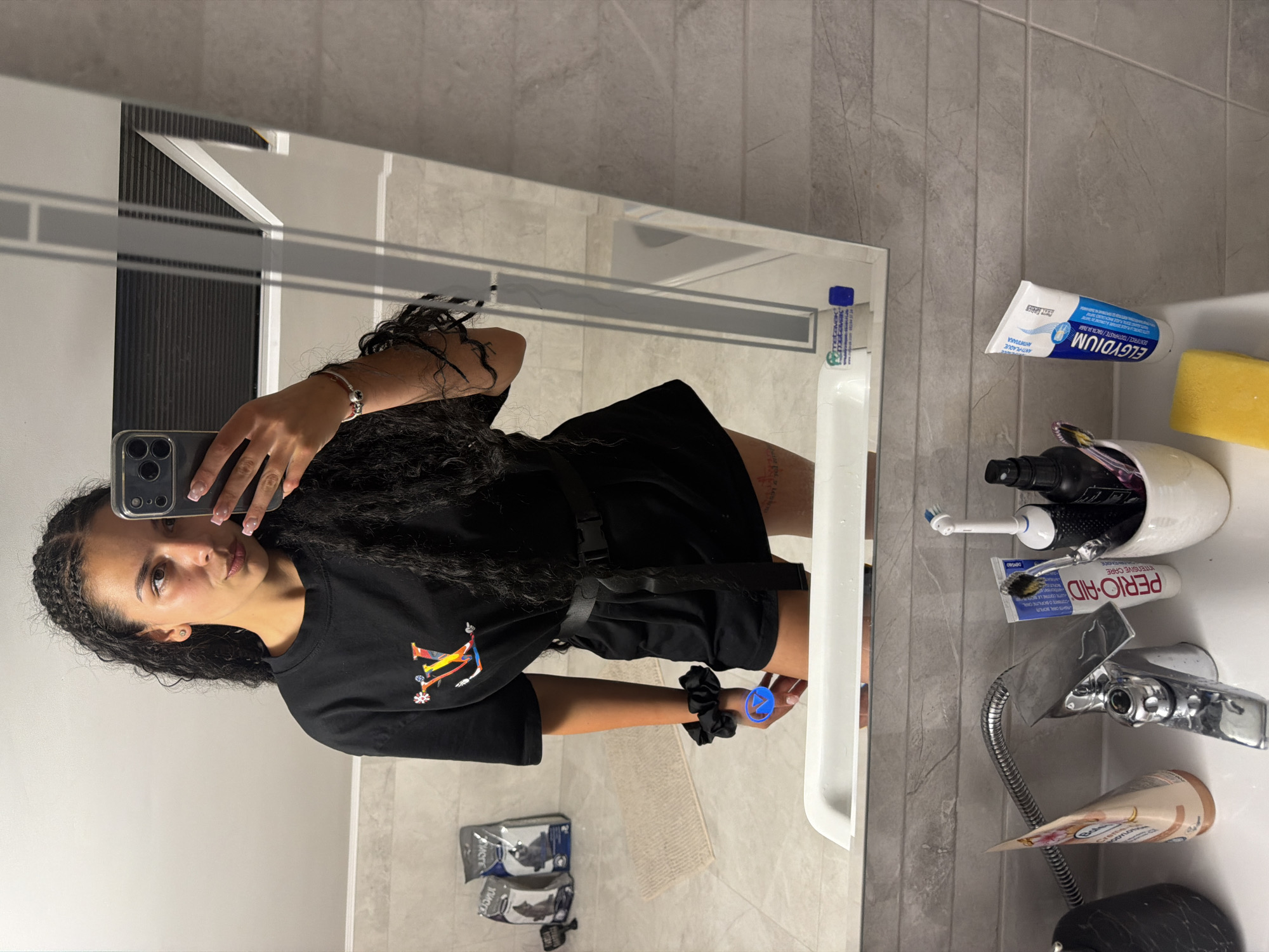 Mirror selfie session in a Gabrovo bathroom, graphic tee and braids.