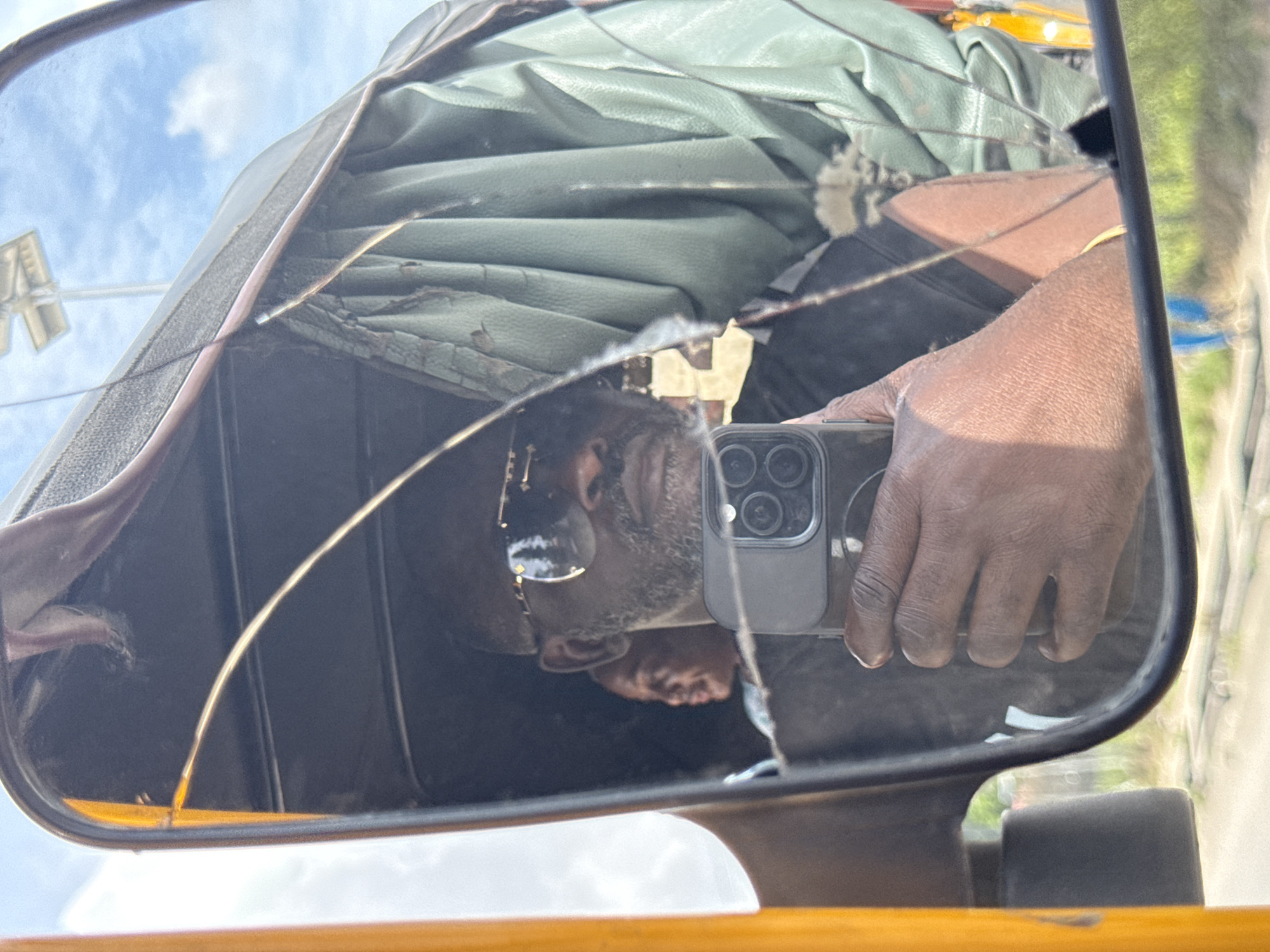 Cracked tricycle mirror reflects smartphone user in Ado, Nigeria