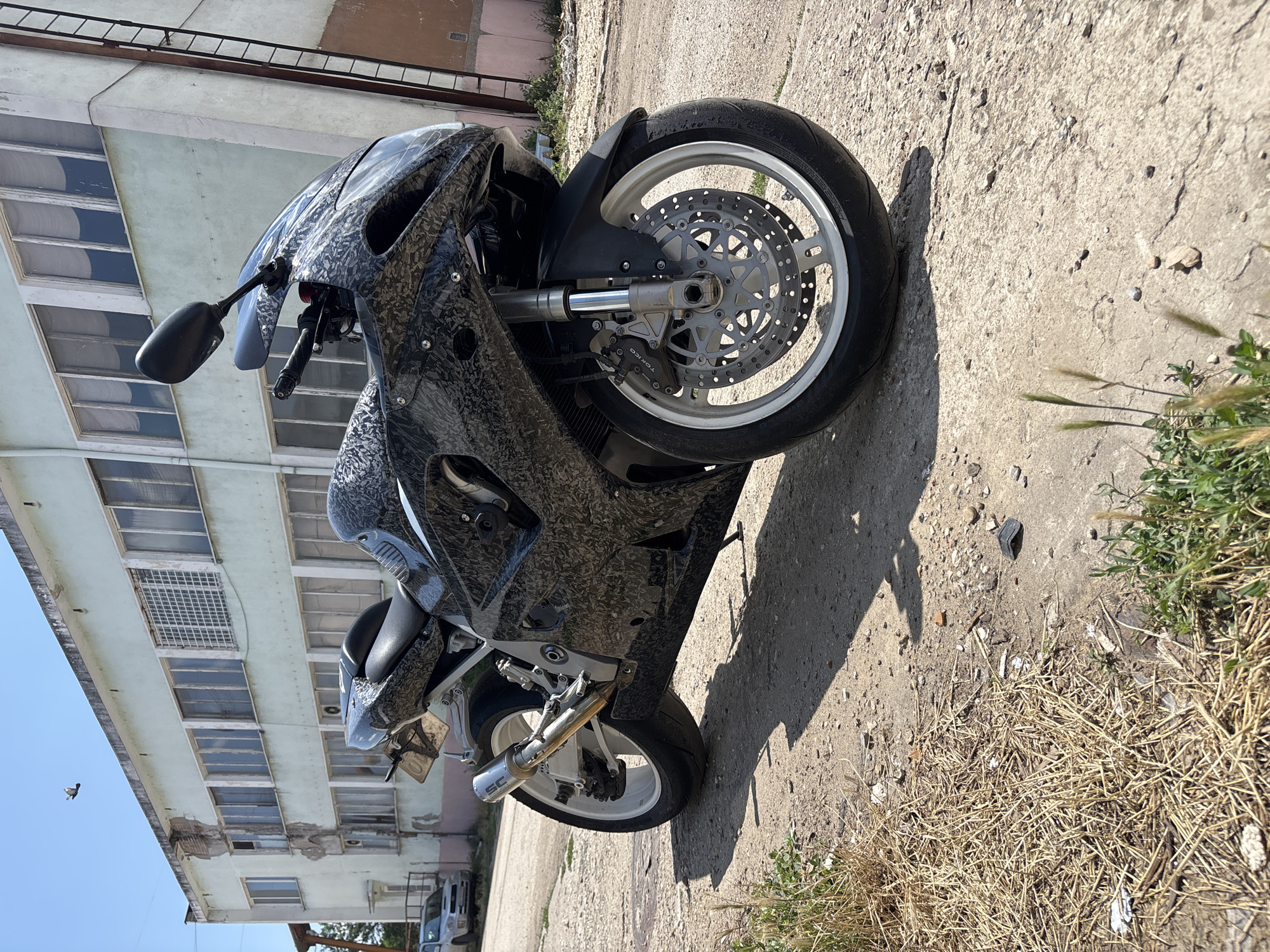 Camo sport bike parked outside weathered industrial building in Pleven