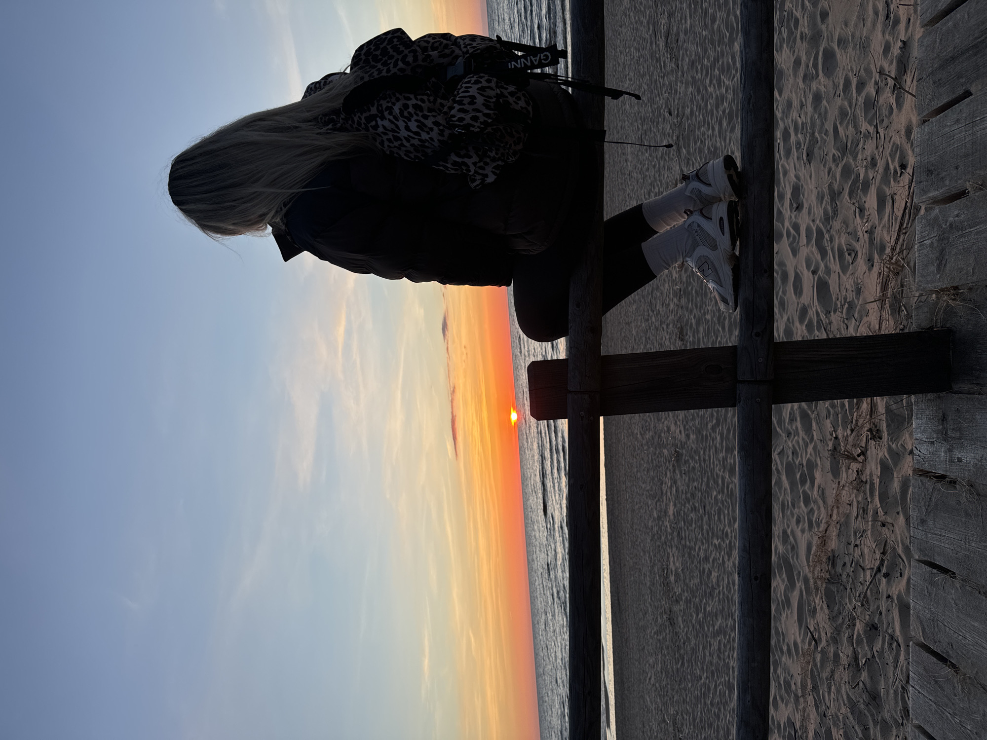 Woman watches Baltic Sea sunset from beach fence in Latvia