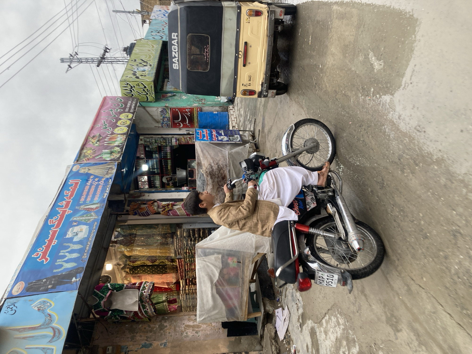 Boy sits on motorcycle near shop in Quetta