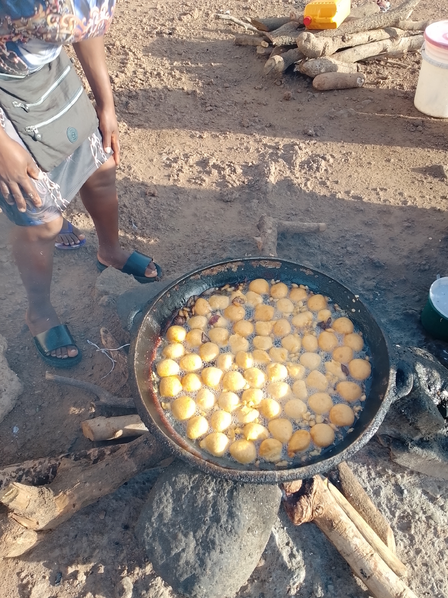 Woman cooks over open fire near busy roadside clearing