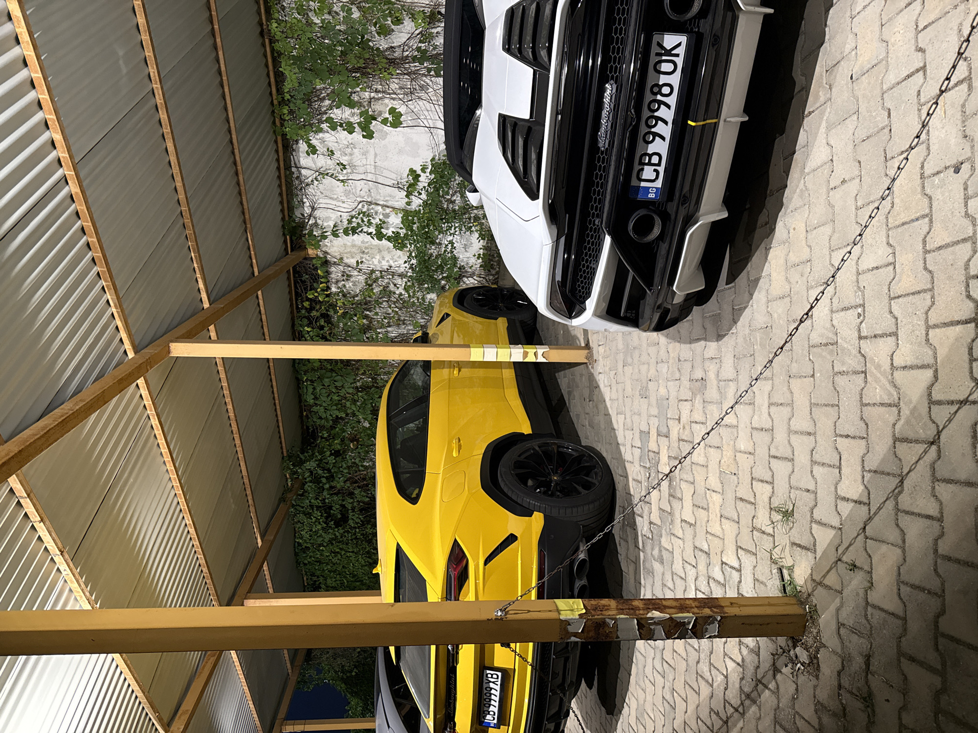Multiple luxury cars parked under a corrugated metal shelter
