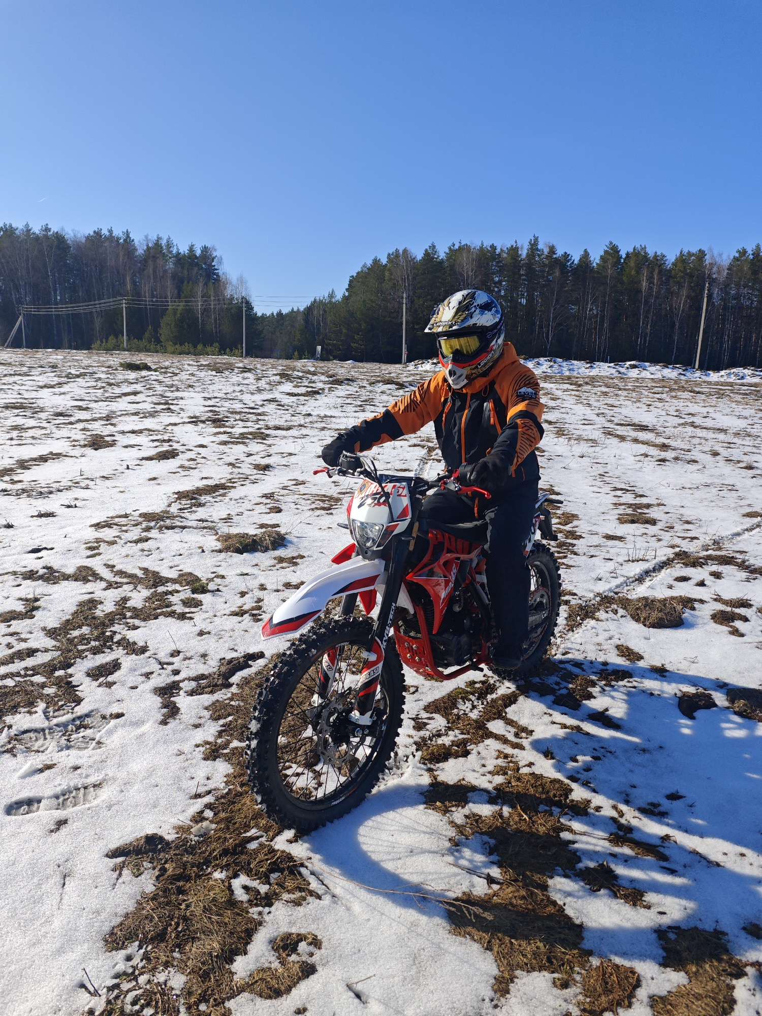 Dirt biker pauses on snowy field in sunny Прикамский
