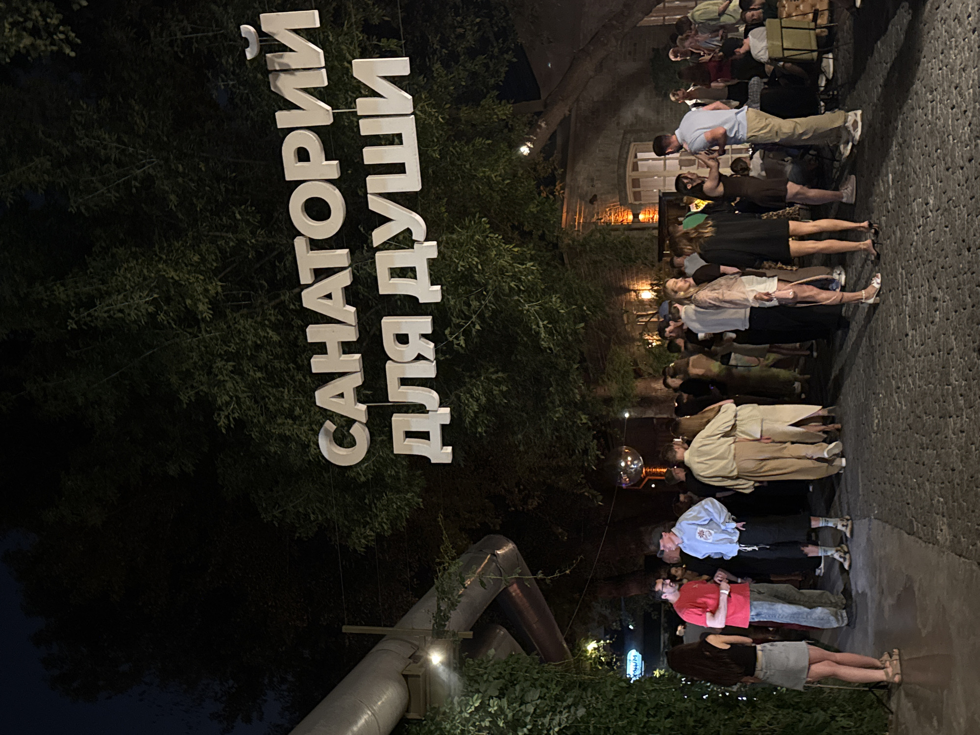 Evening crowd gathers under glowing Cyrillic letters at outdoor event