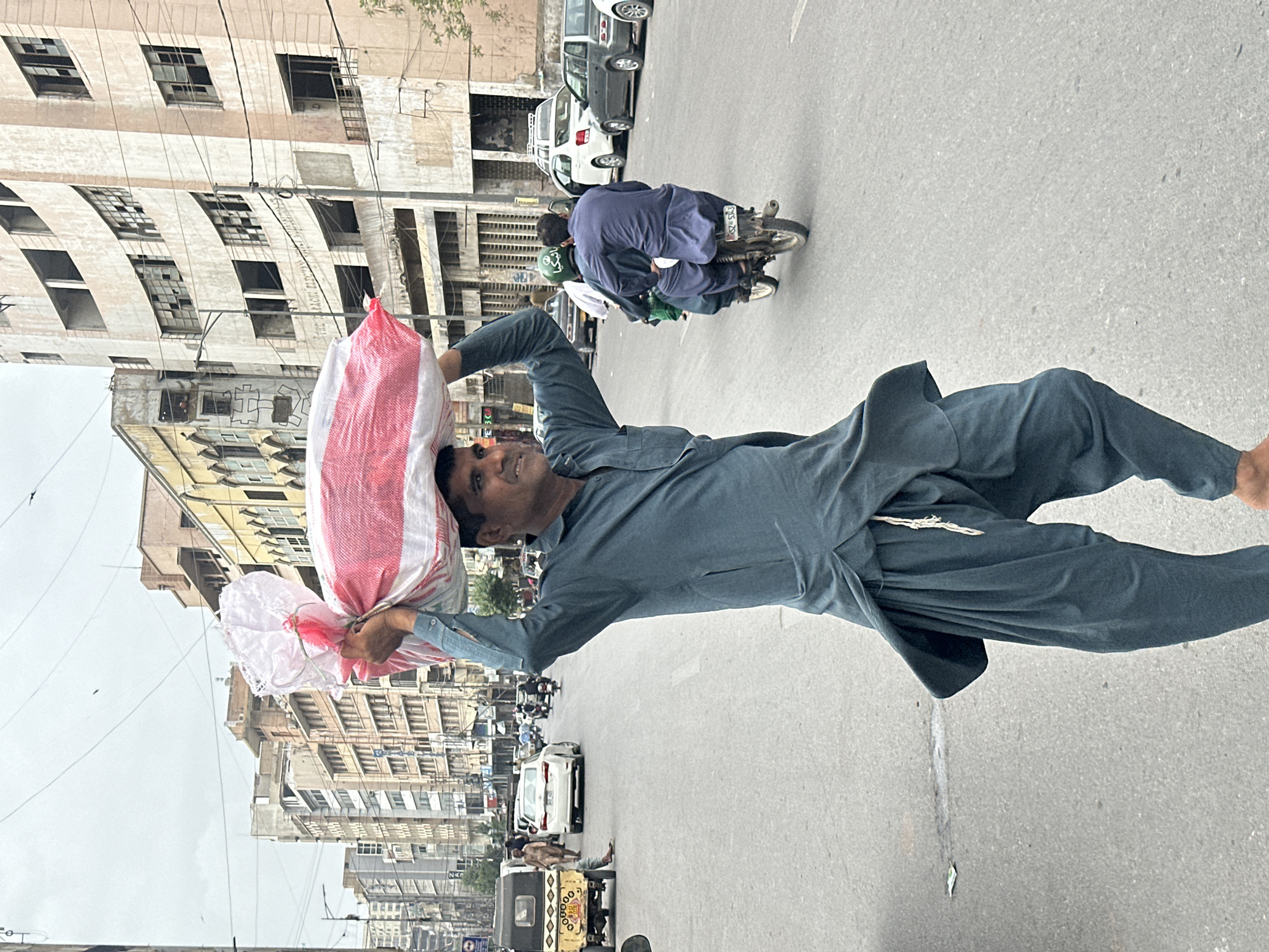 Carrying a large striped bag across a Karachi street