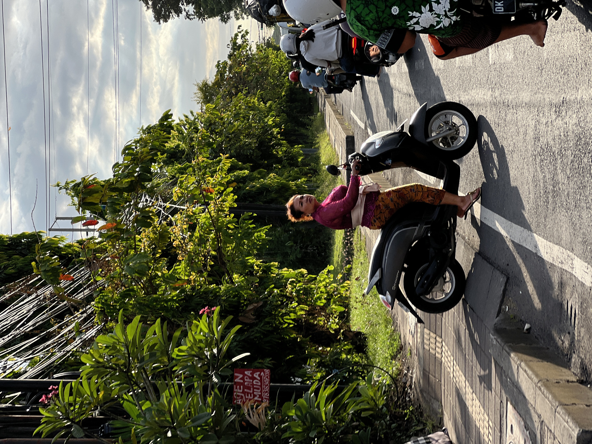 Woman sits on parked scooter in Denpasar street