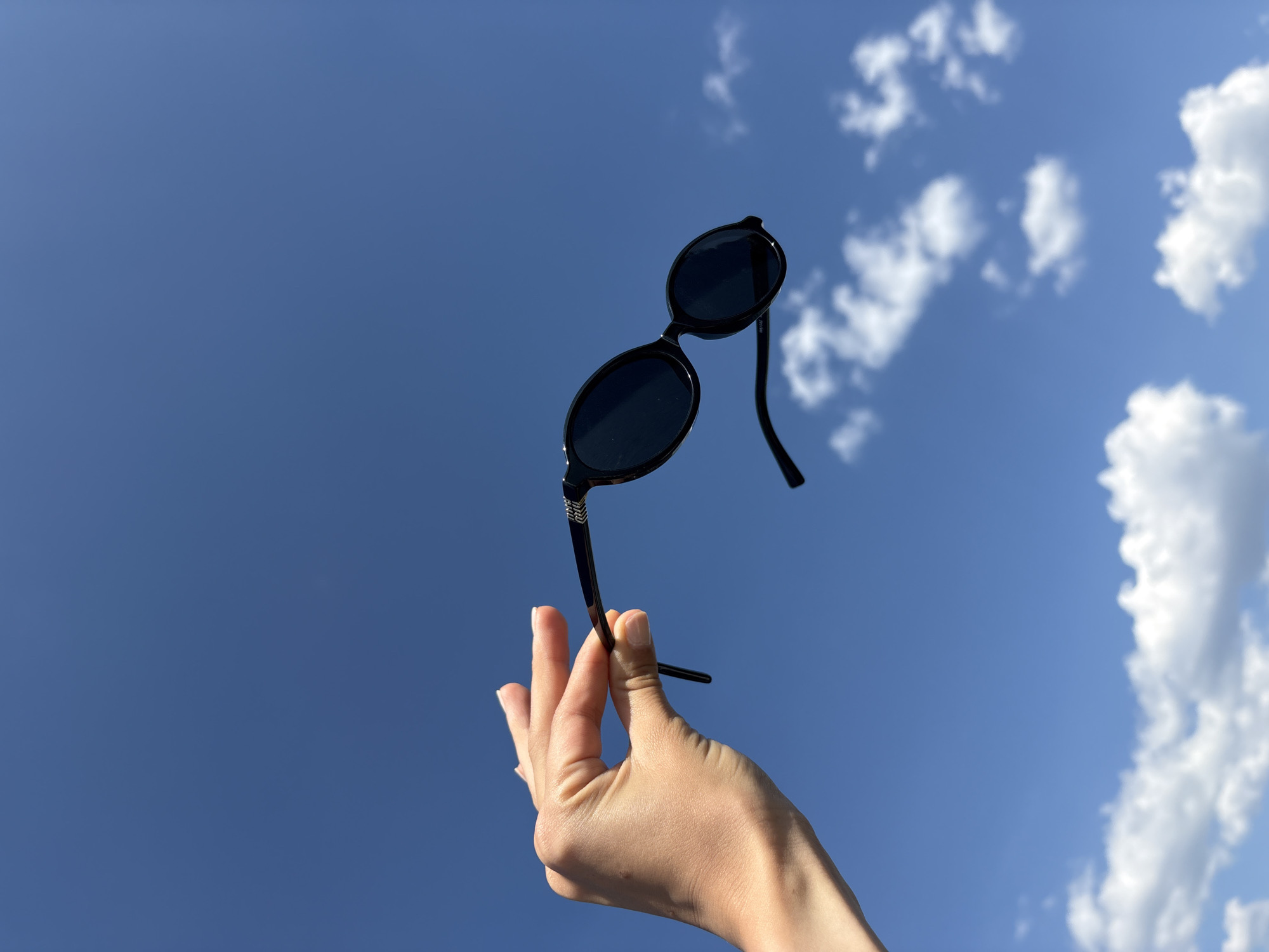 Hand holds sunglasses against blue sky in Valle de Bravo