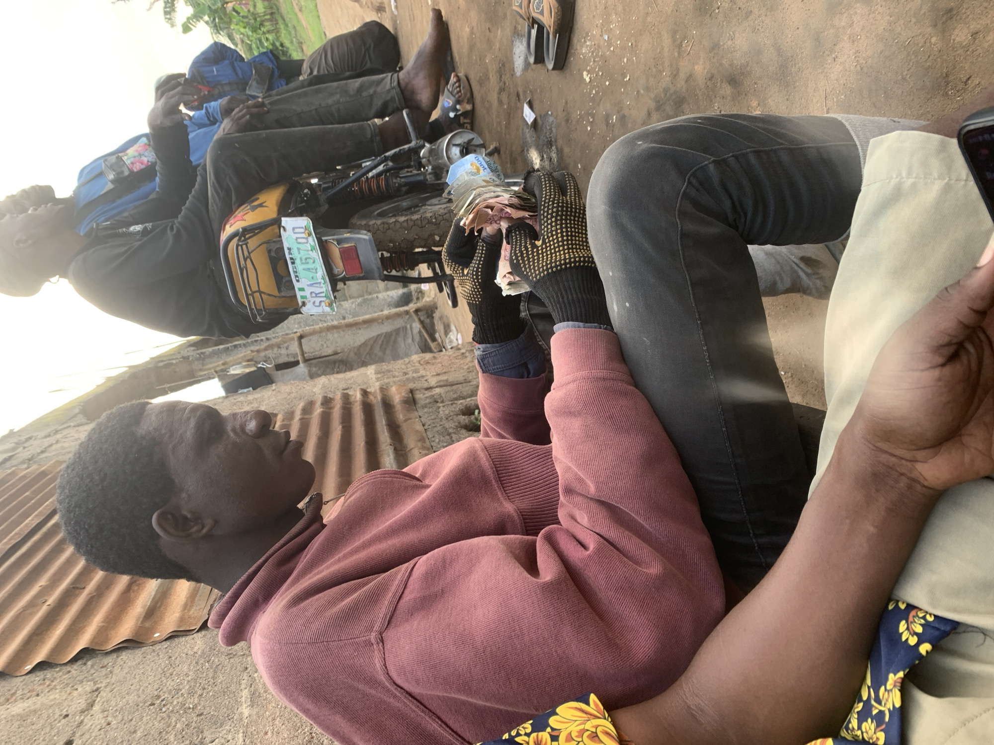 Roadside motorcycle repair and cash exchange in Shagamu, Nigeria