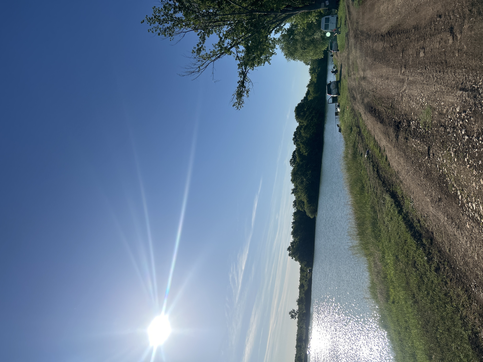 Sunny waterway scene with vegetation and dirt road documented