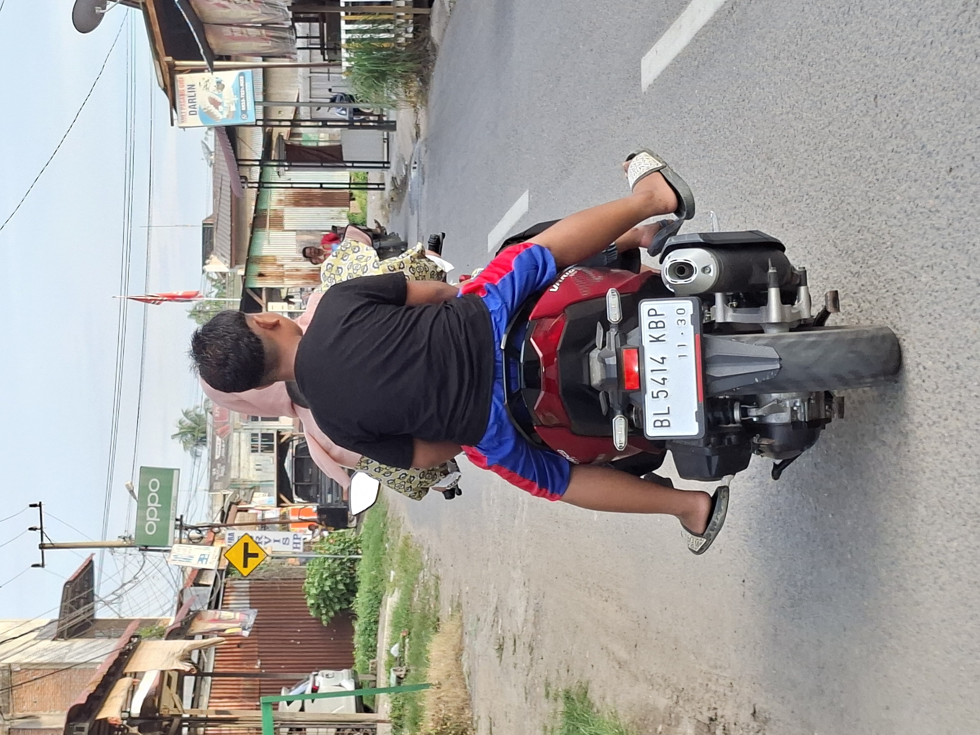 Man rides red moped through Keudegeudong, Indonesia