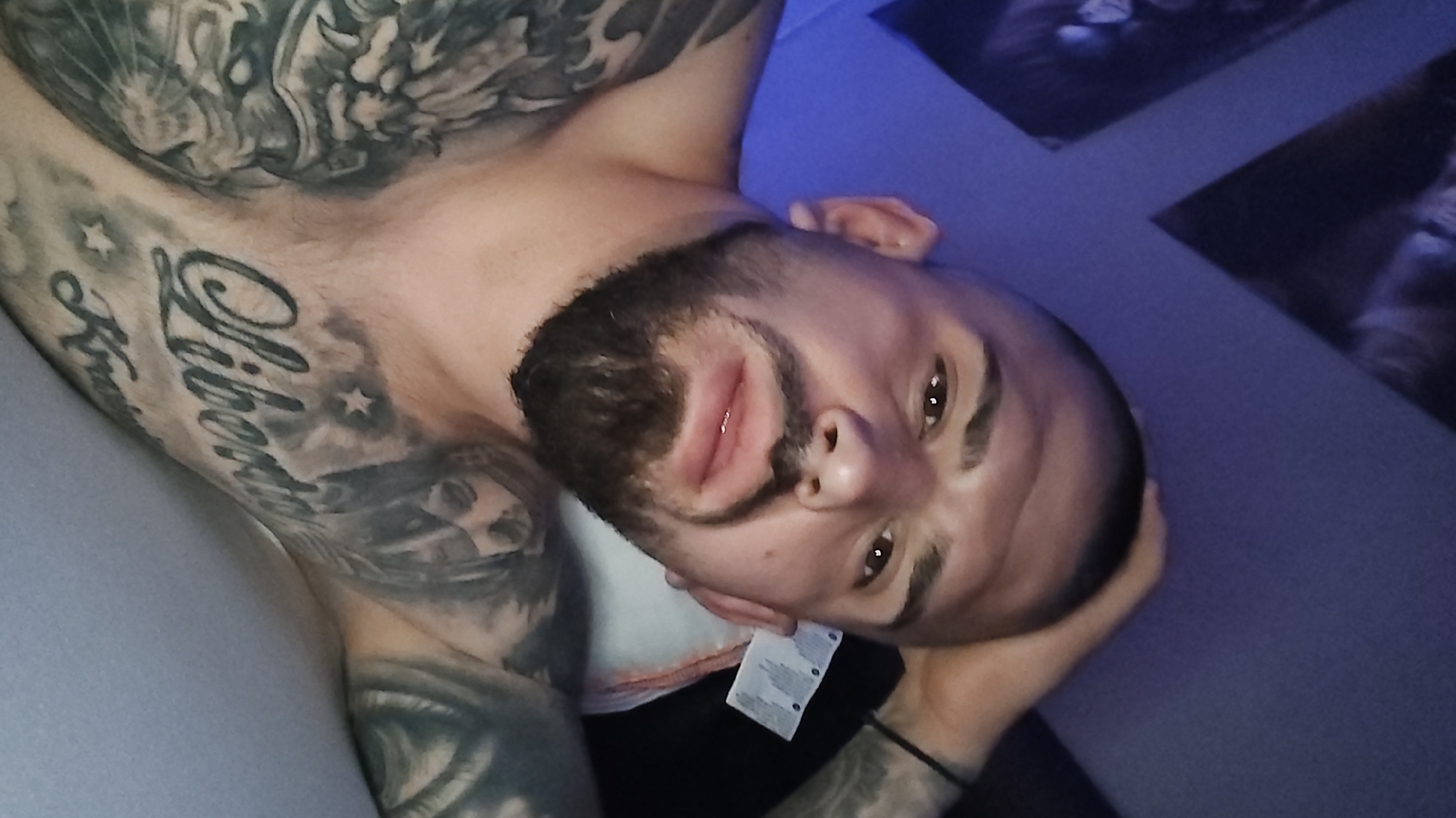 Tattooed man rests in blue-lit bedroom in Venlo