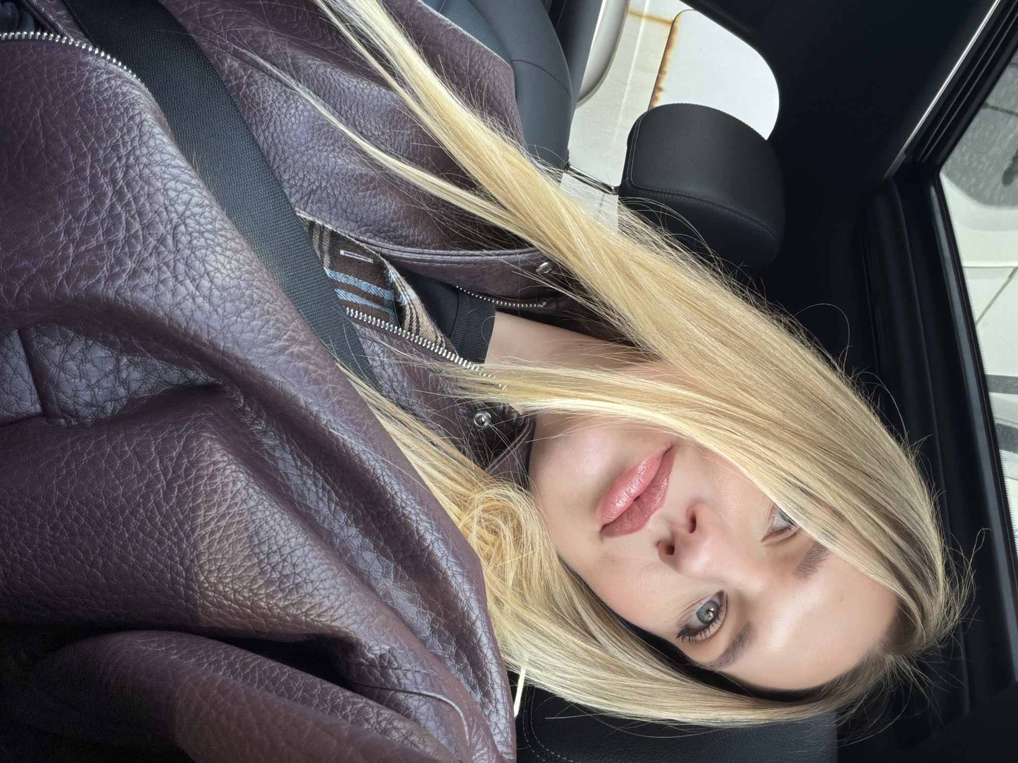Woman applies lip tint in car passenger seat, Riga