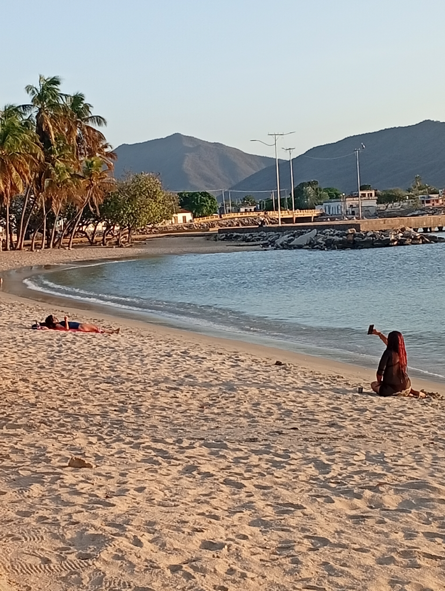 Woman documents sunset beach evening with boats and historic landmarks