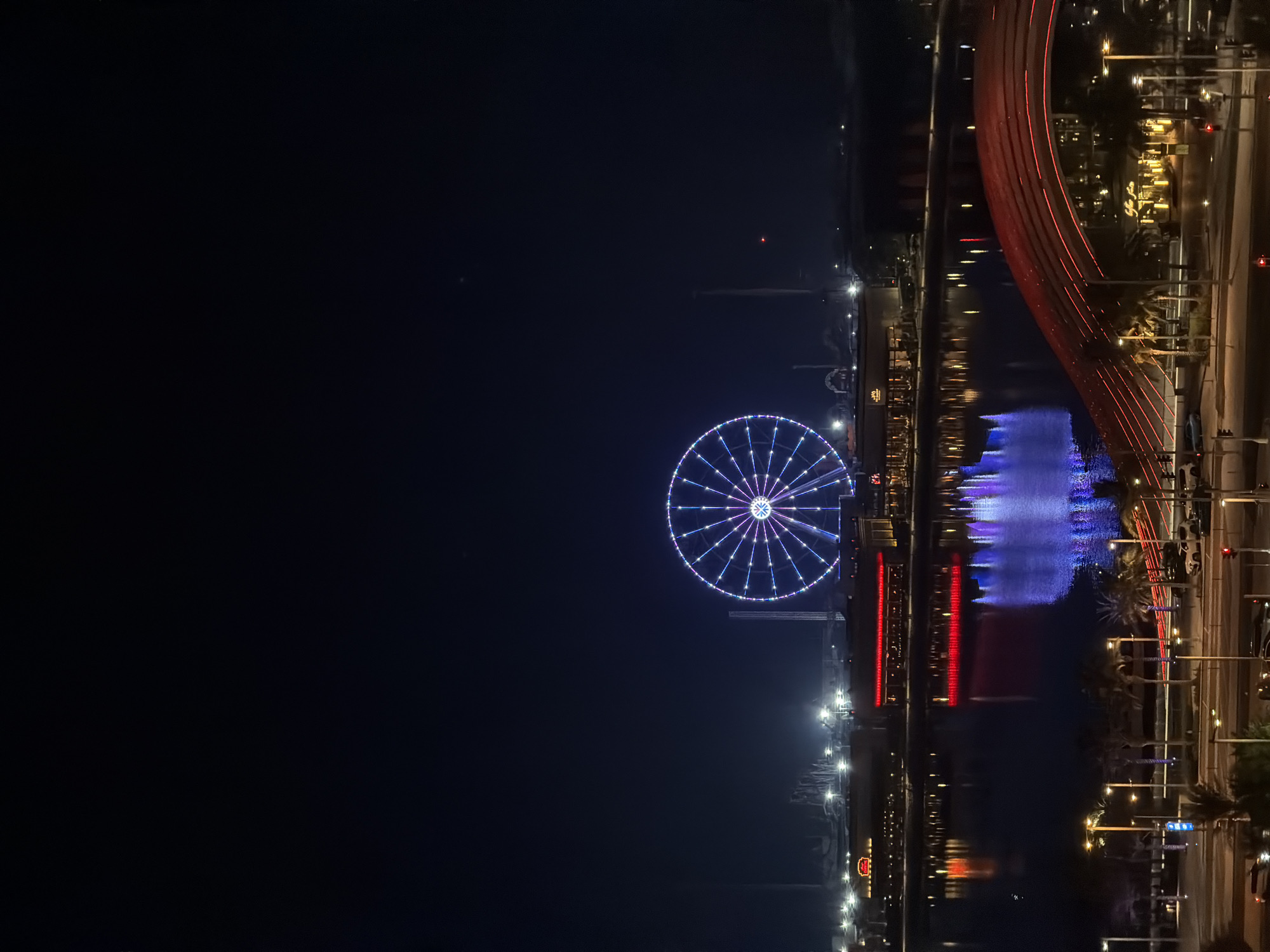 Ferris wheel and glowing skyline along a city waterfront at night