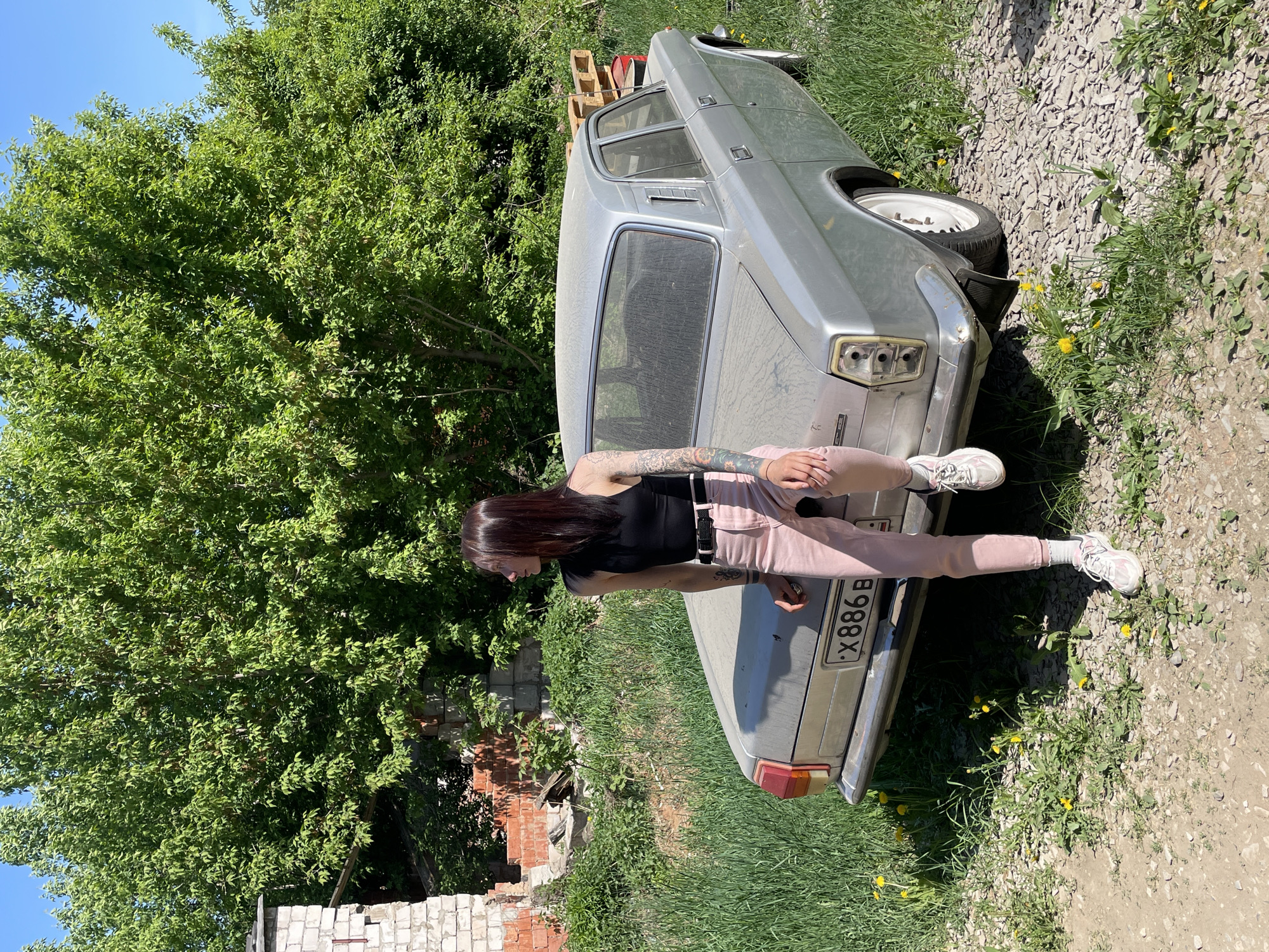 Woman leans against dirty silver car in Chemoshur