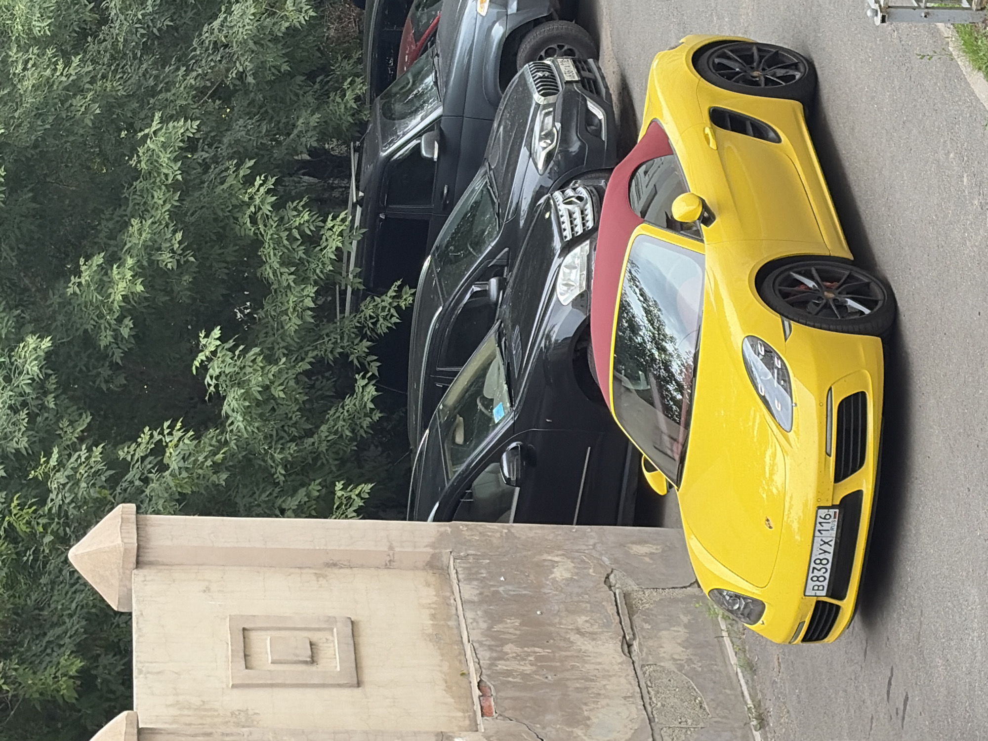 Yellow Porsche Boxster with red top parked on city street