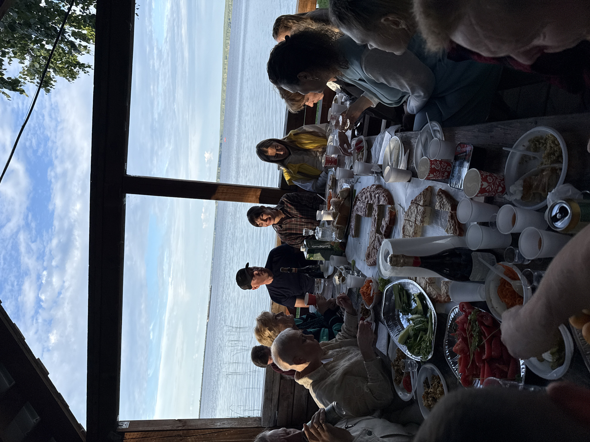 Outdoor lakeside meal under a wooden pavilion with a group.