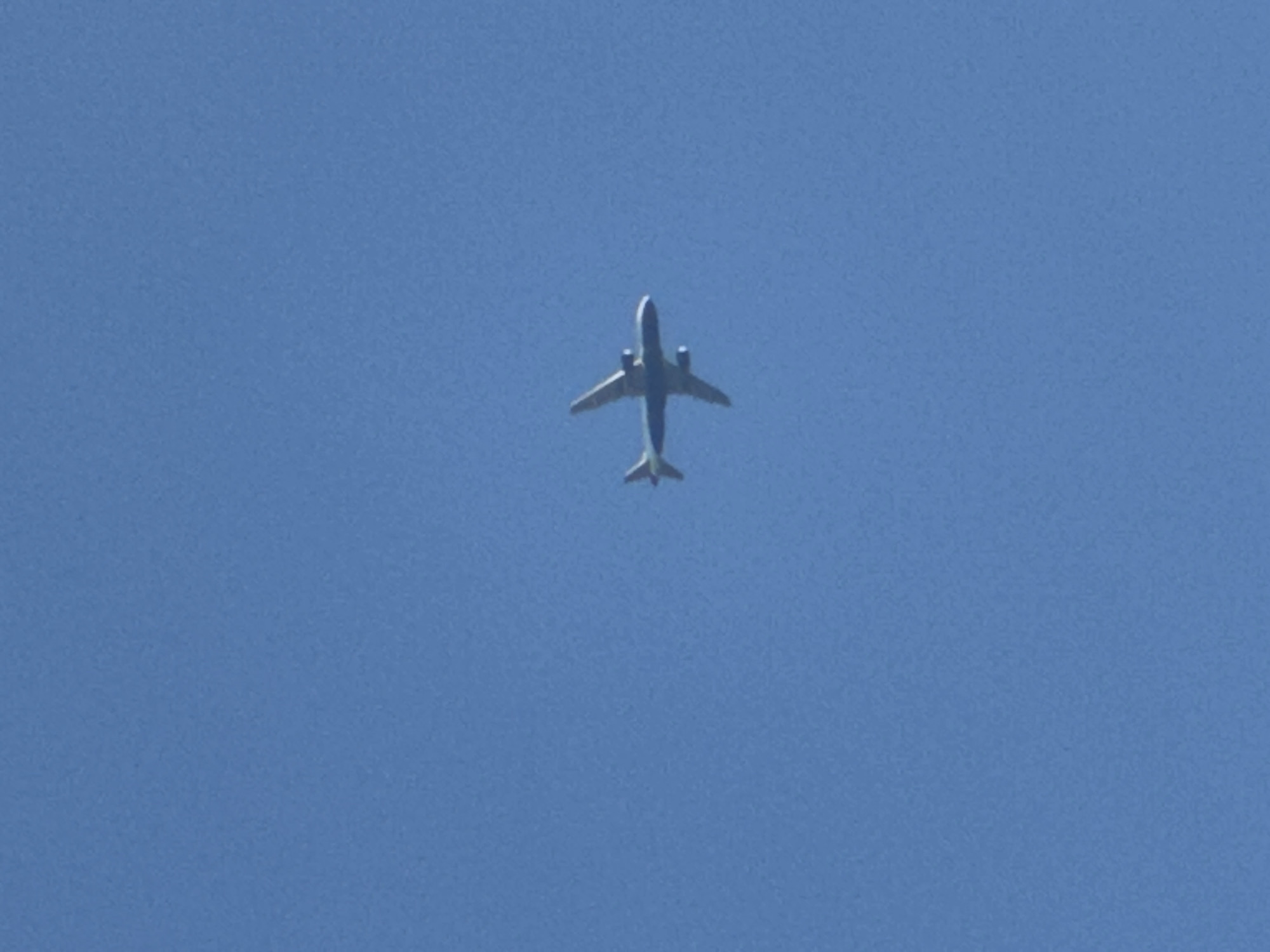 Orange-accented commercial jet cruises through clear London skies