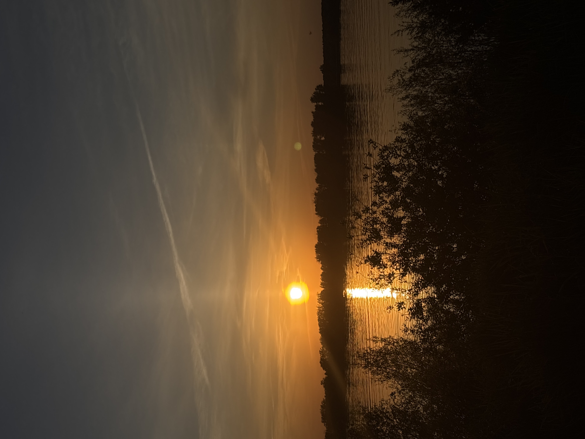 Sunset observed over water near wooded area May 21