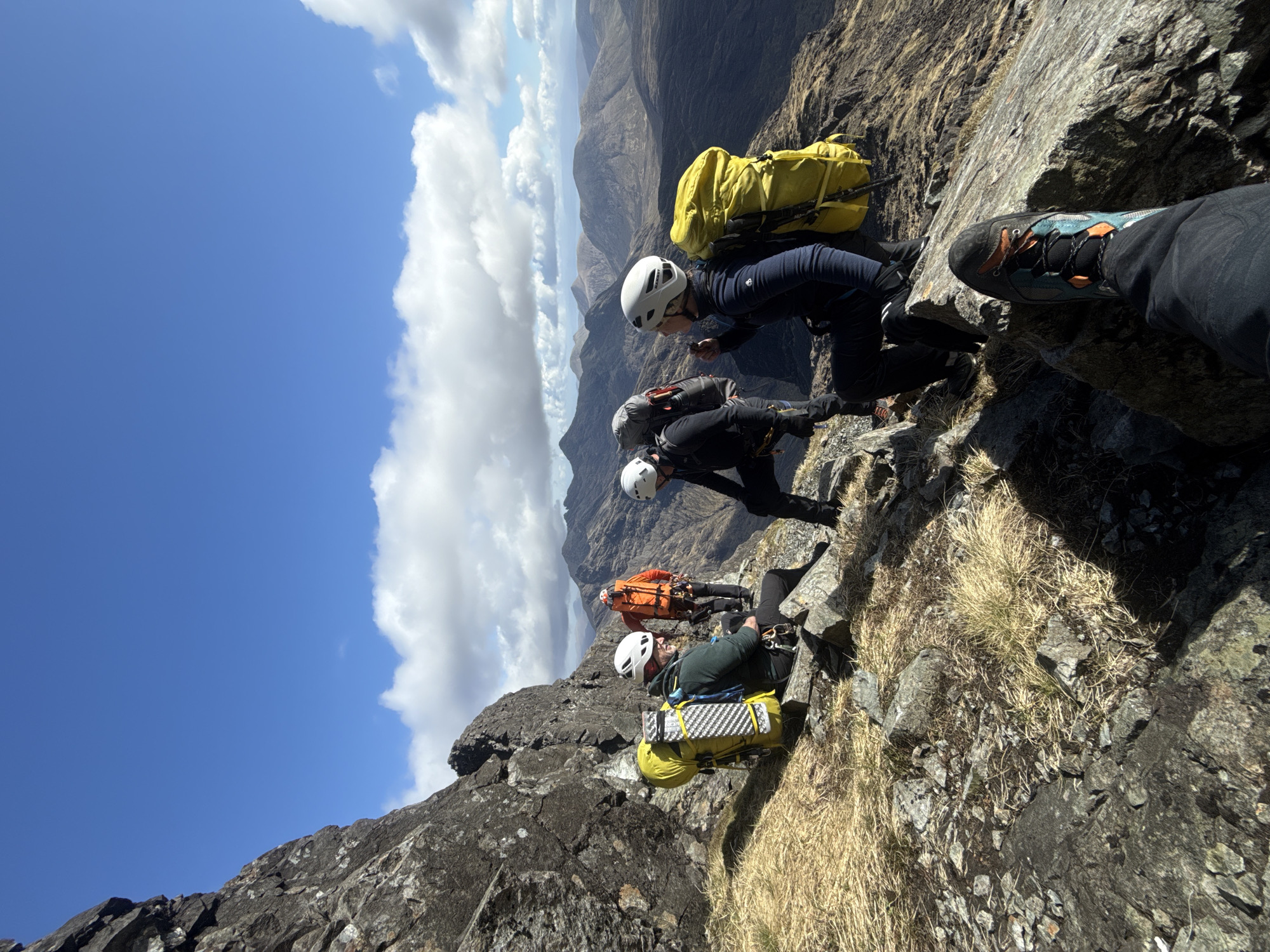 Helmeted hikers traverse rocky mountain ridge in formation