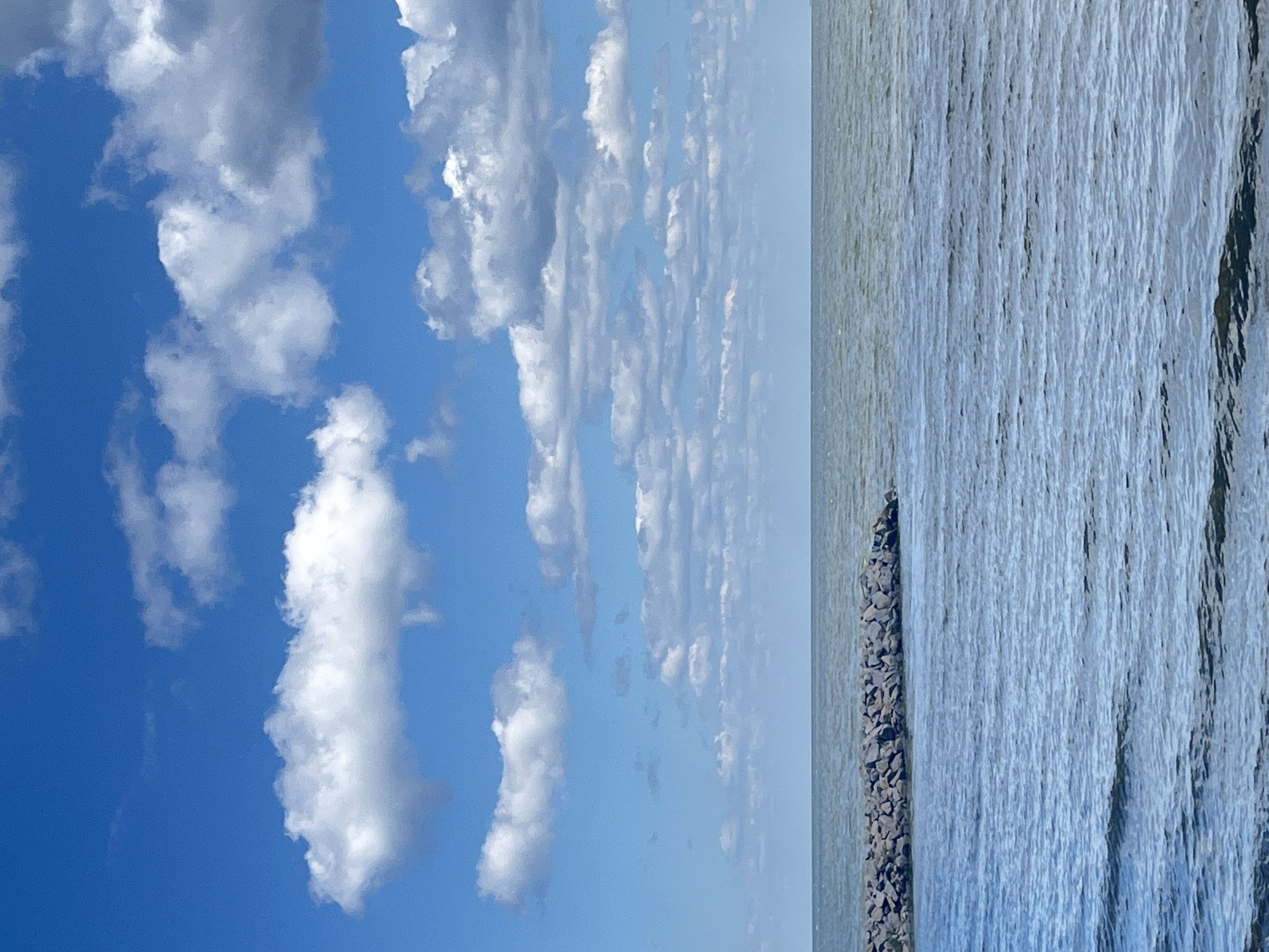 Stone breakwater meets open water under a partly cloudy sky