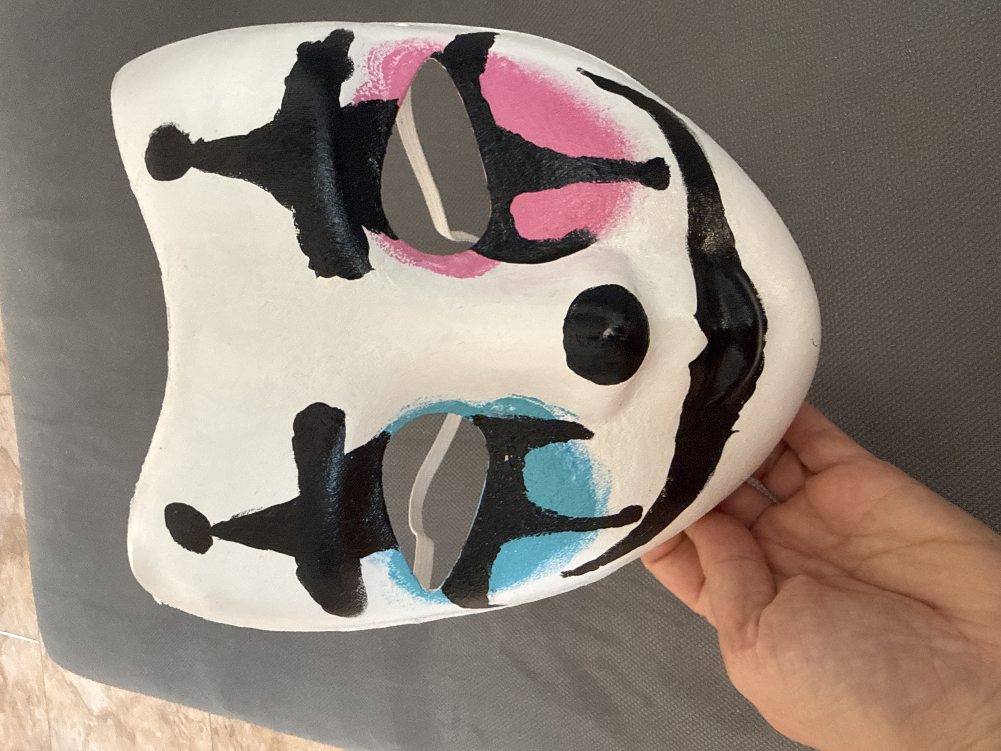 Person holds decorated white mask with colored markings
