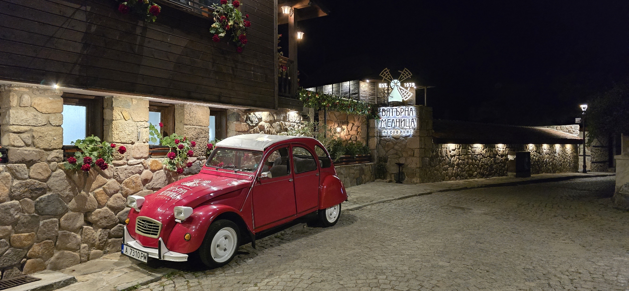 Red 2CV parked on cobblestones outside a flower-lined Sozopol building