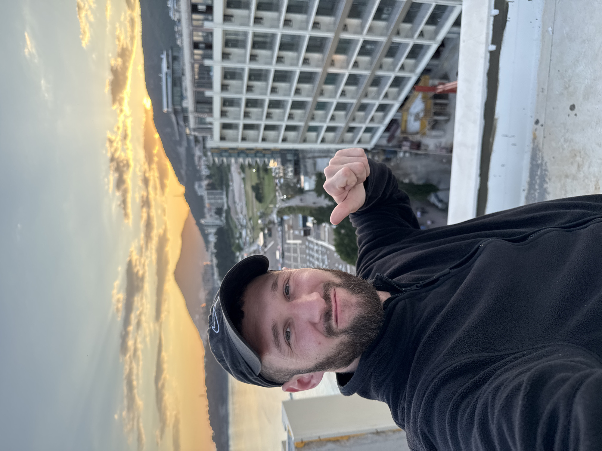 Man gives thumbs-down from rooftop during city sunset