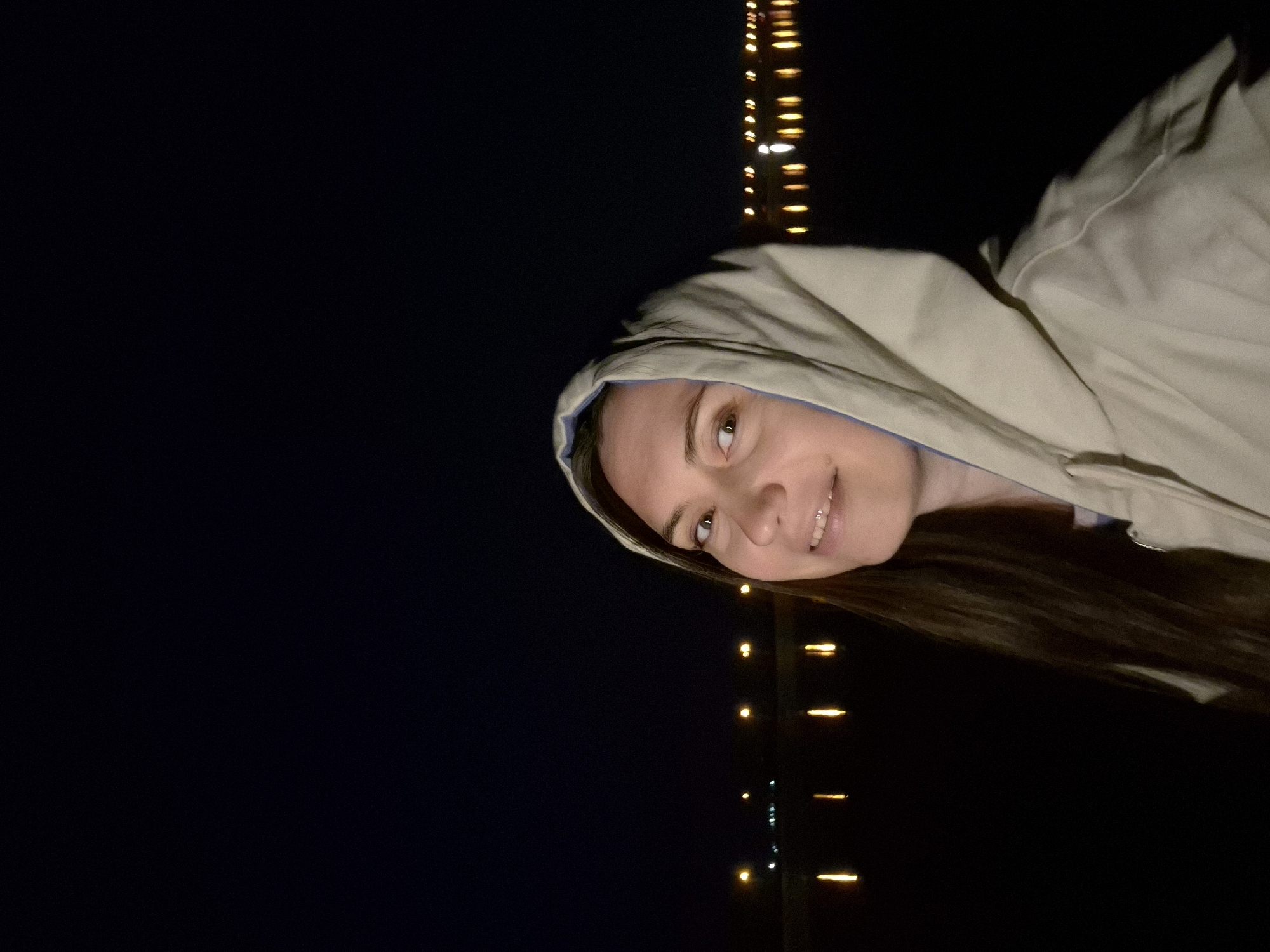 Woman in hooded jacket photographed smiling near yellow lights