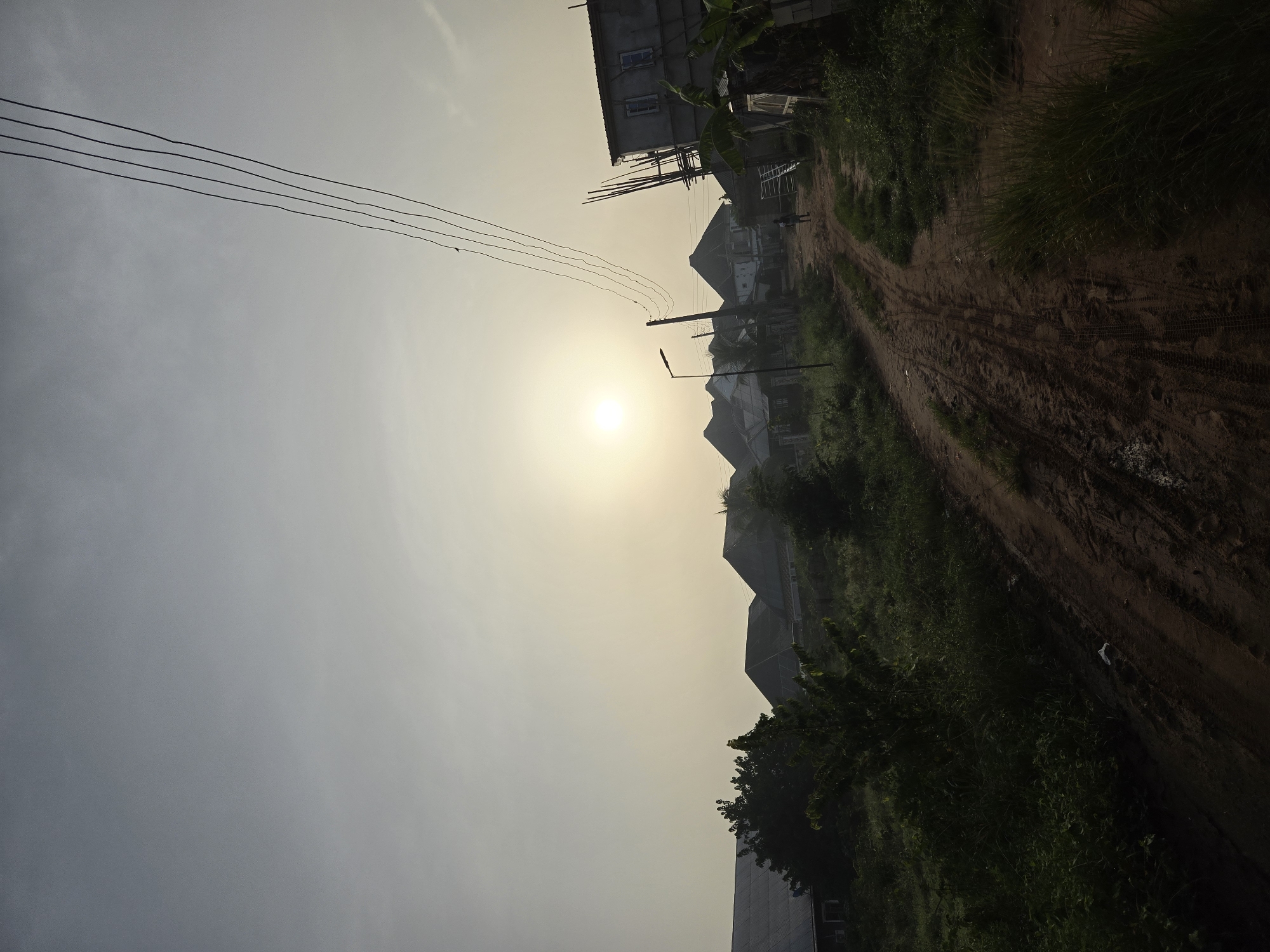 Morning haze obscures sun over dirt road to buildings
