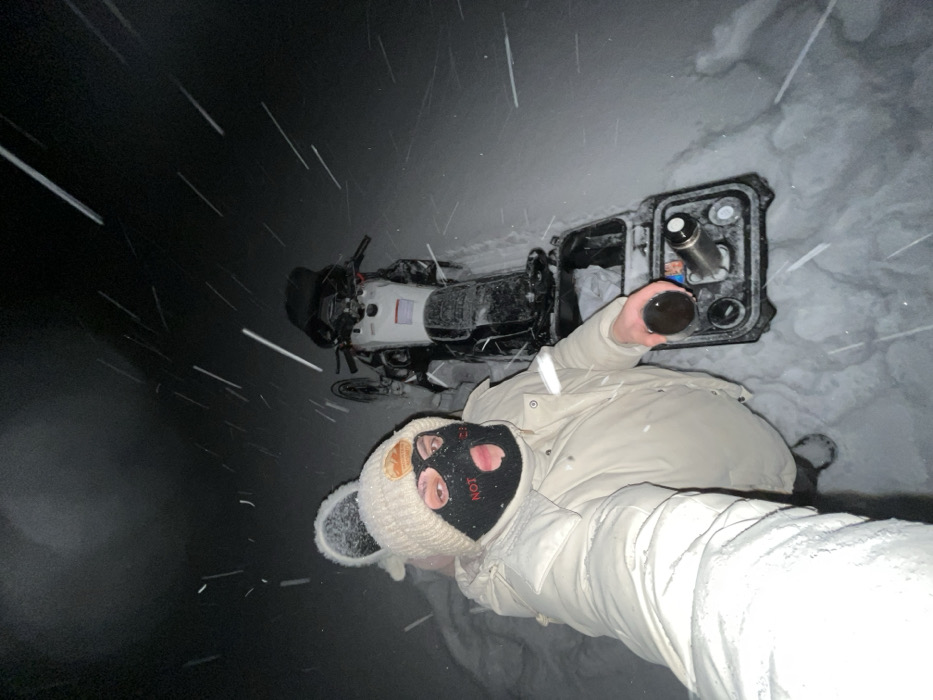 Winter traveler with motorcycle pauses during heavy snowfall in Russia