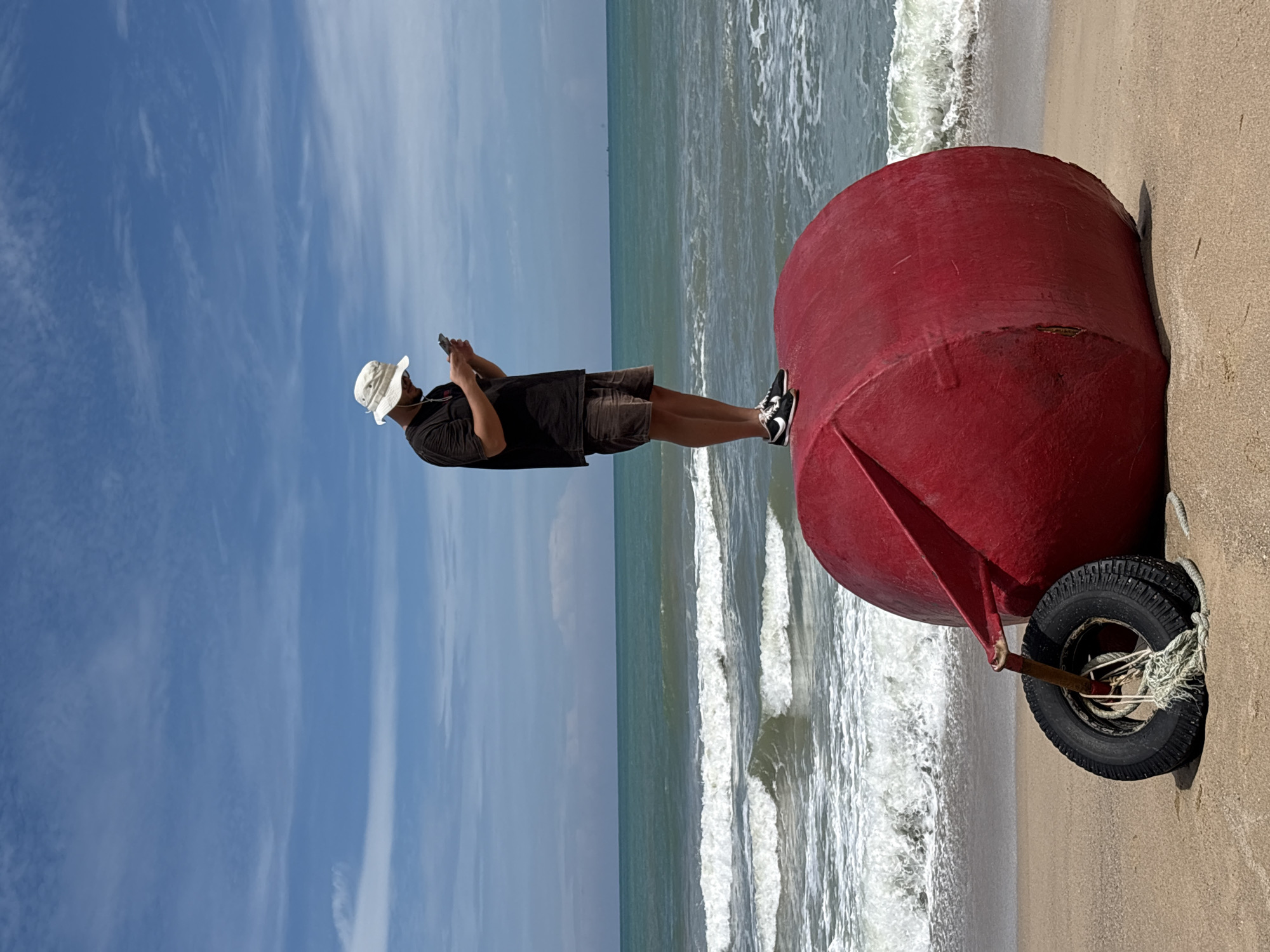 Man explores Choeng Thale beach at dawn, poses on red buoy