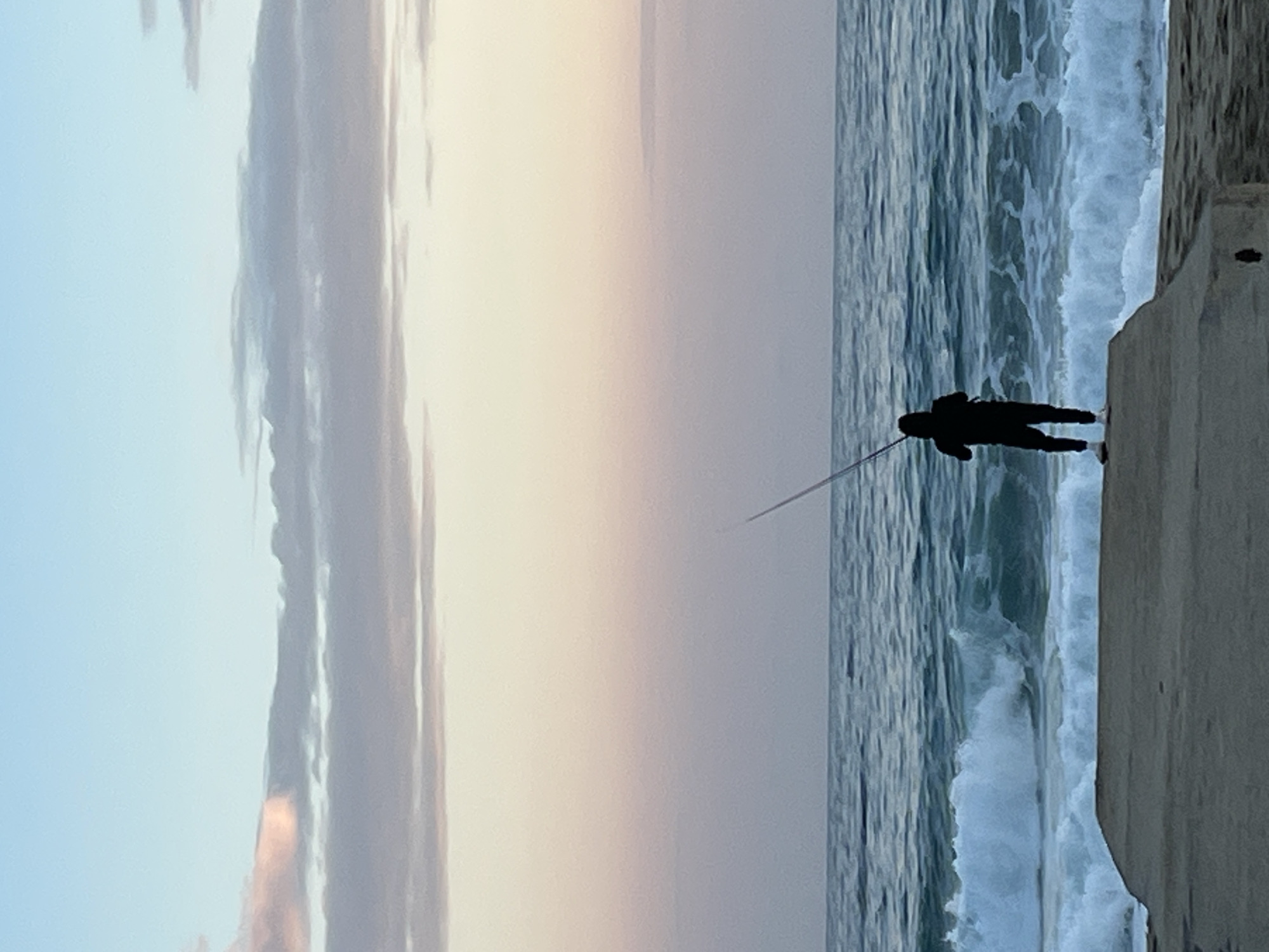 Lone angler fishes from Alanya embankment under colorful evening sky
