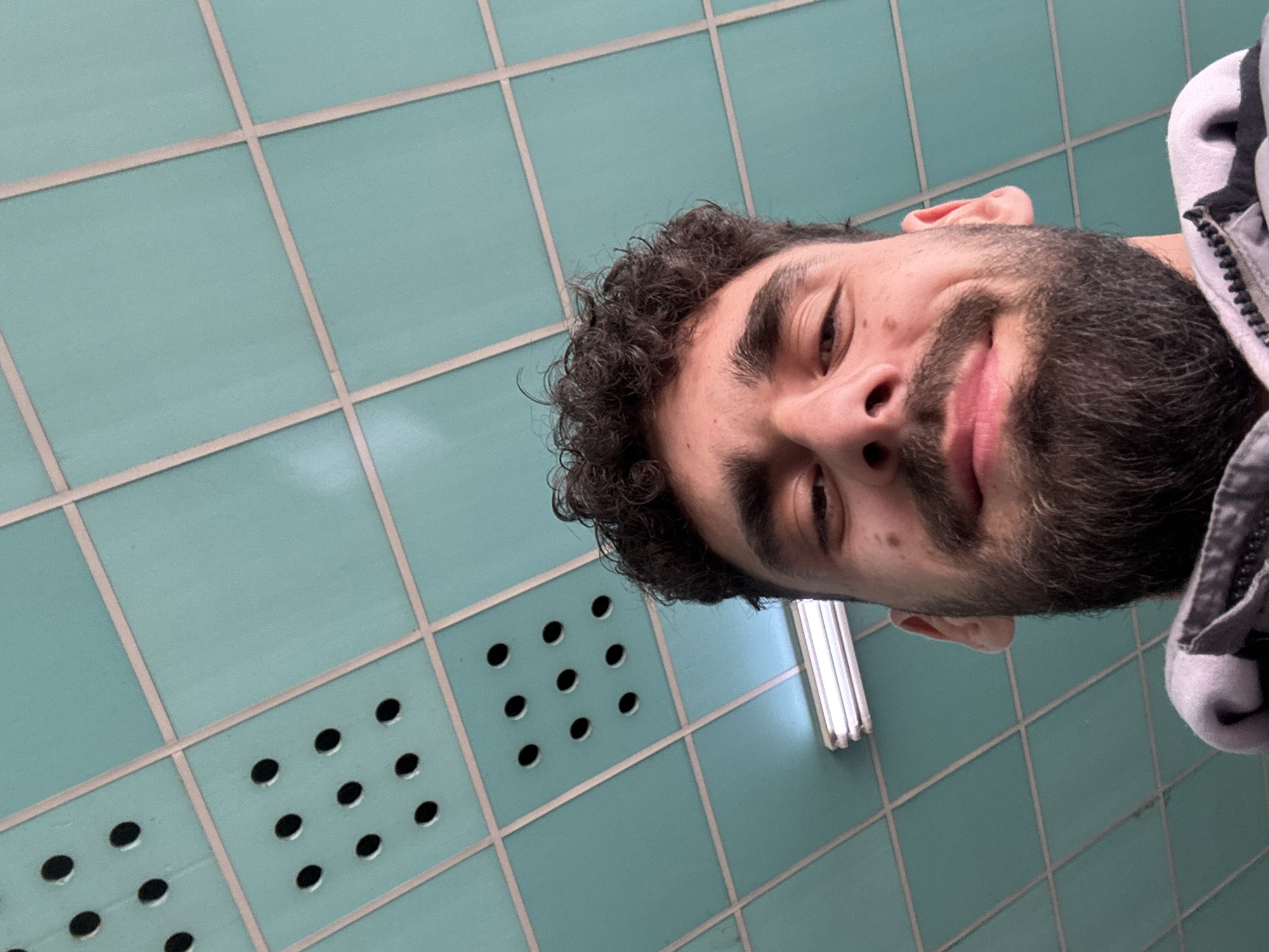 Man in gray hoodie takes selfie against tiled wall