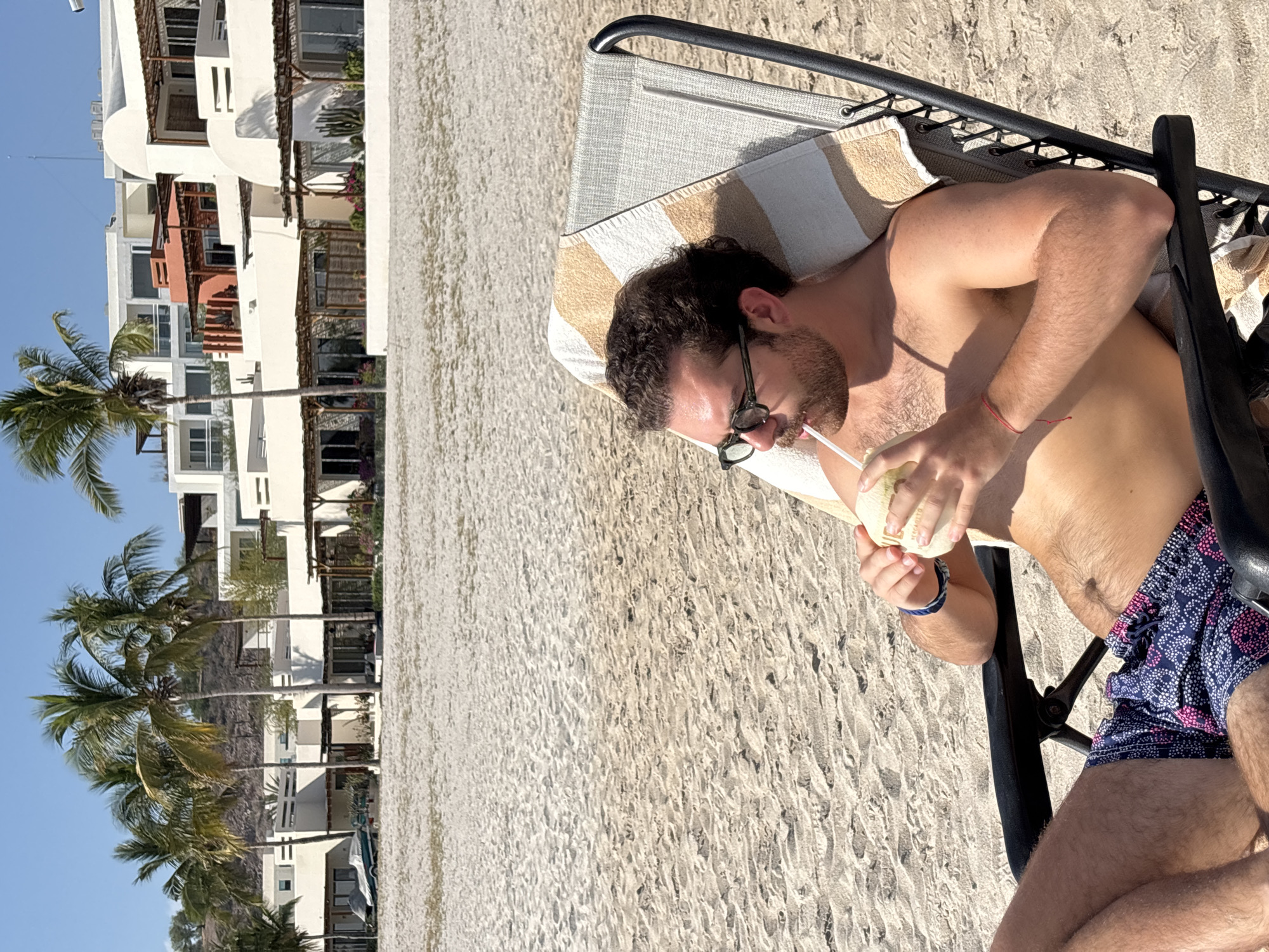 Tourist enjoys coconut drink on beach chair in La Paz
