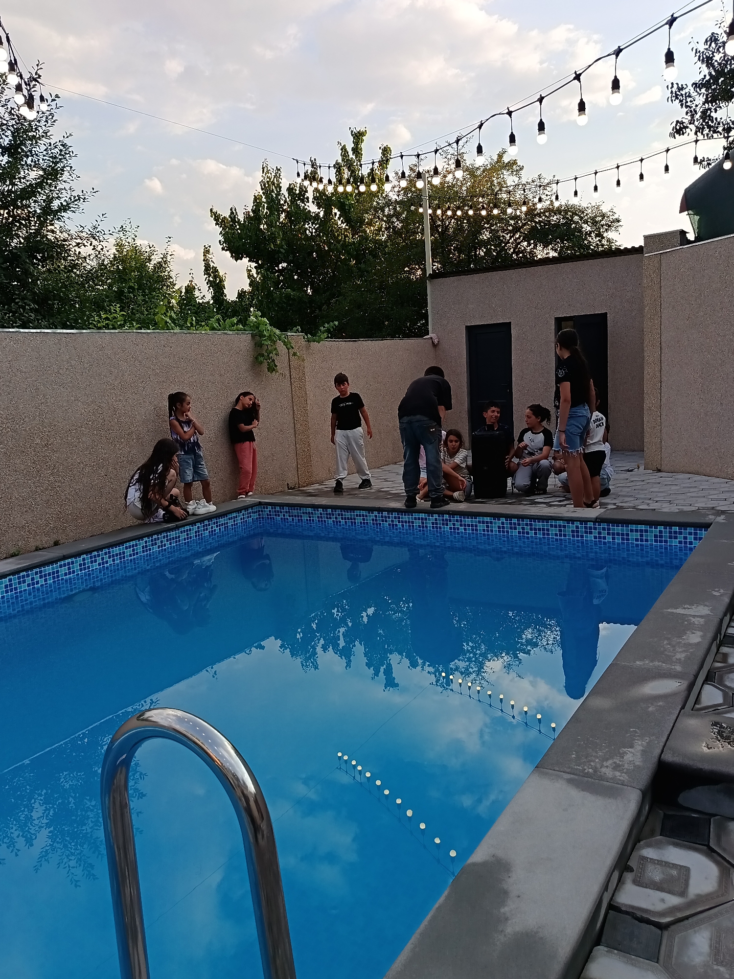 Kids gather poolside with music, lights, and a relaxed backyard vibe.