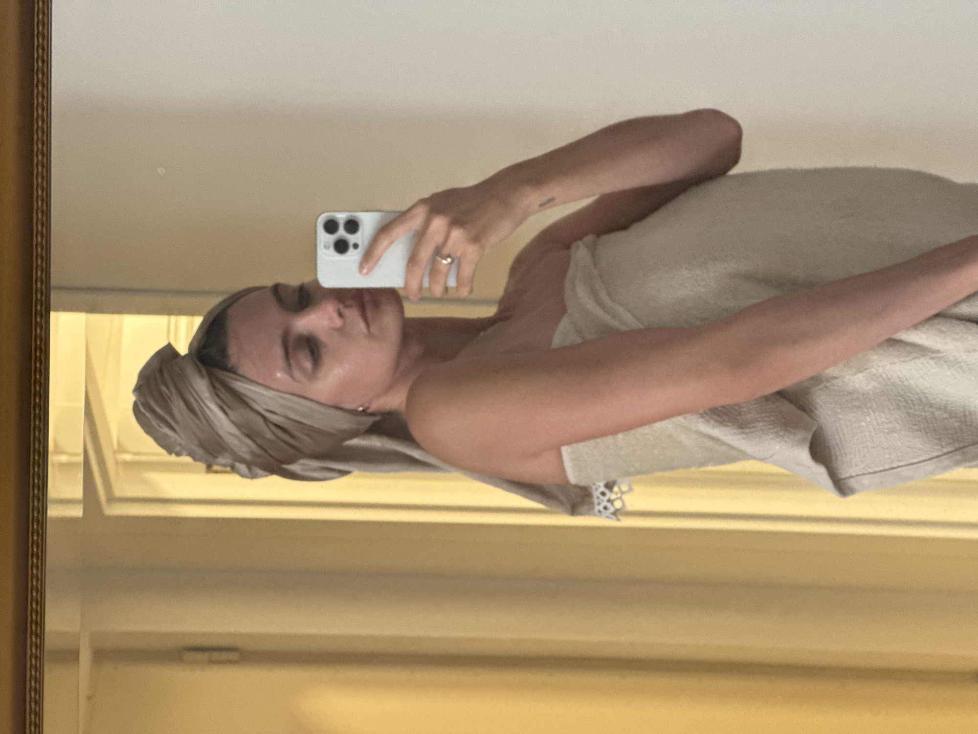 Woman takes towel-wrapped mirror selfie with white phone