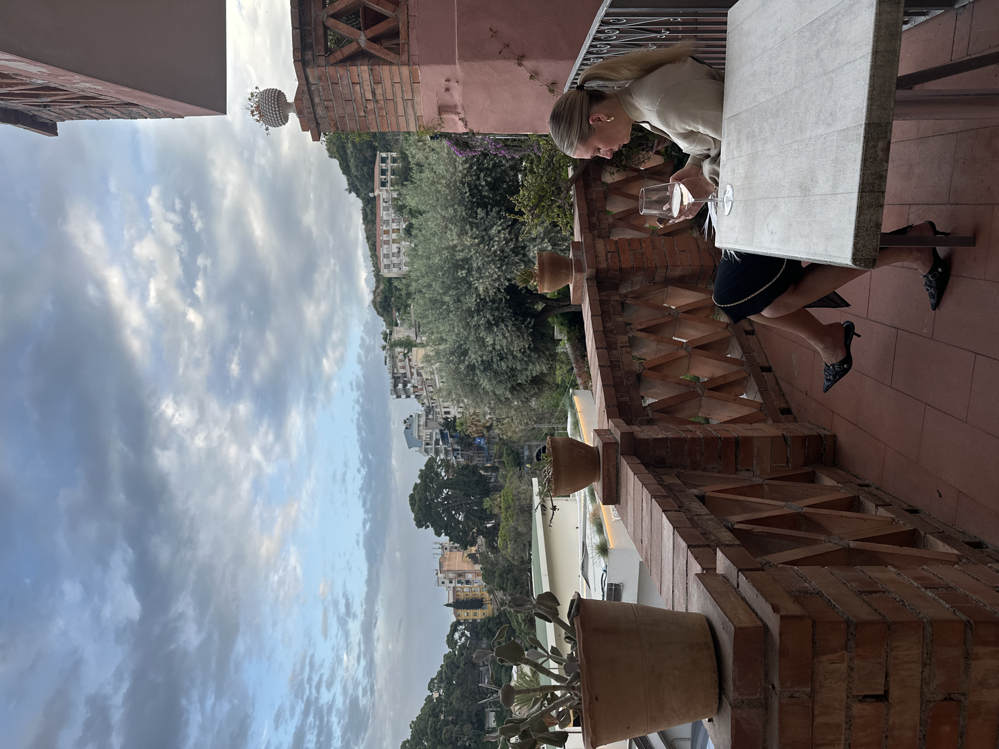 Woman enjoys drink on Taormina terrace overlooking scenic hills