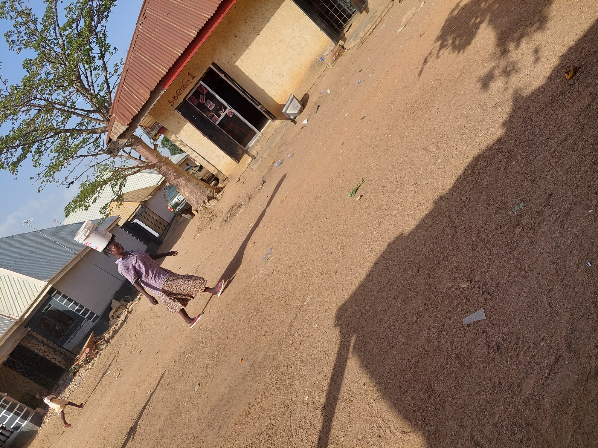 Woman carries water bucket on dusty Nigerian street