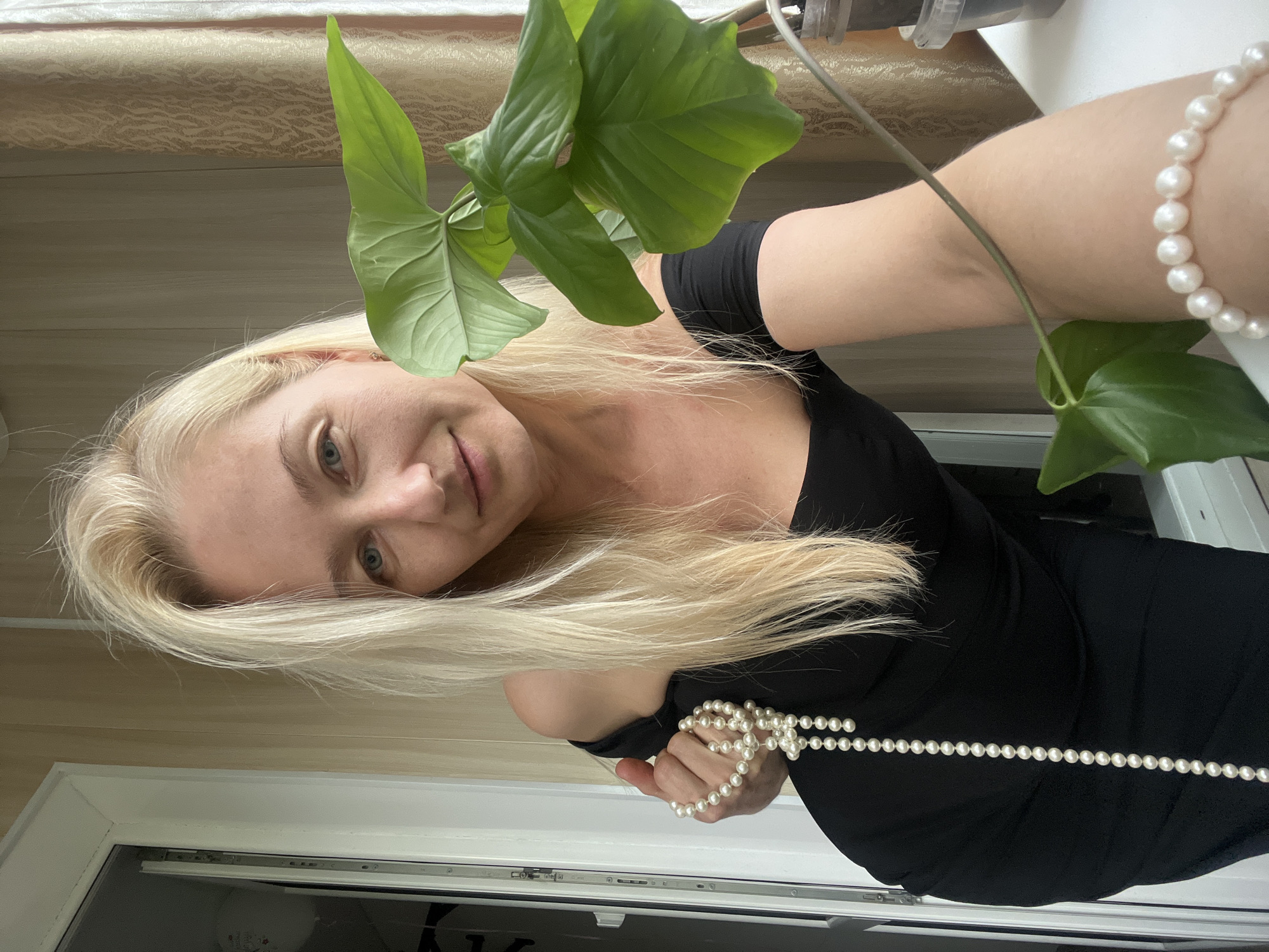 Woman tends plant while holding pearls in Ulyanovsk home