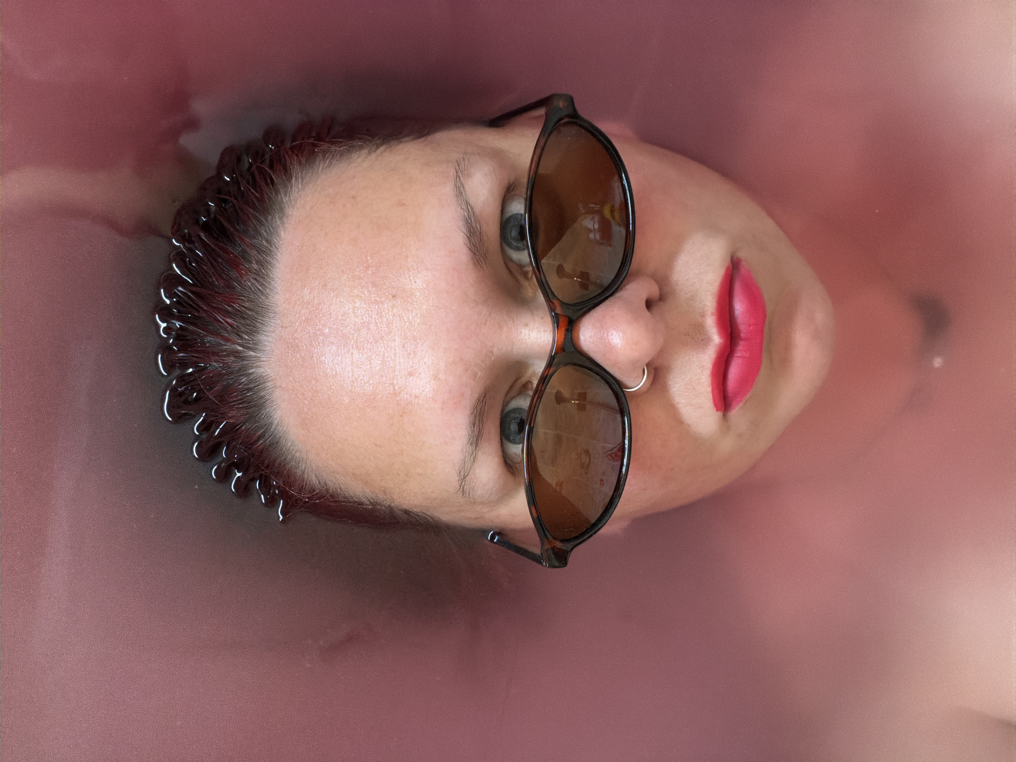 Woman observed bathing in pink water wearing sunglasses